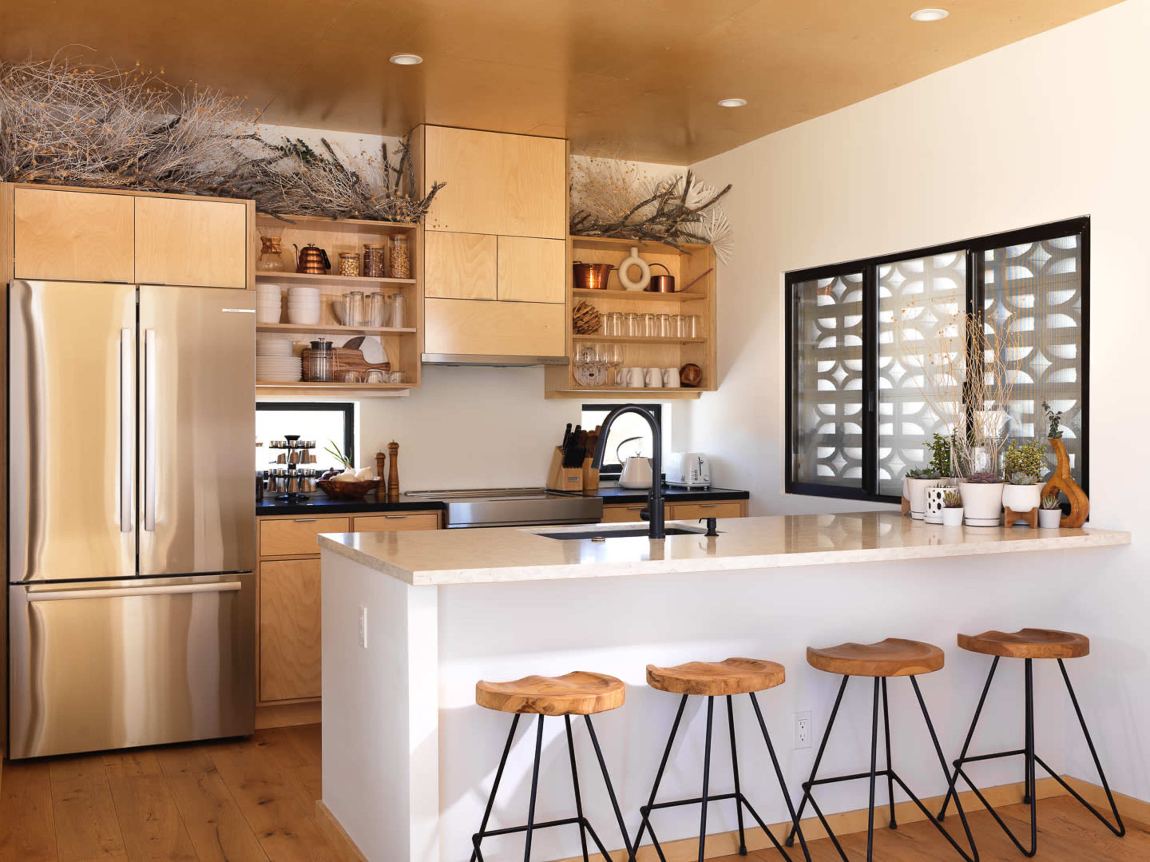 A modern kitchen features wooden cabinetry, a stainless steel refrigerator, and a countertop with bar stools.