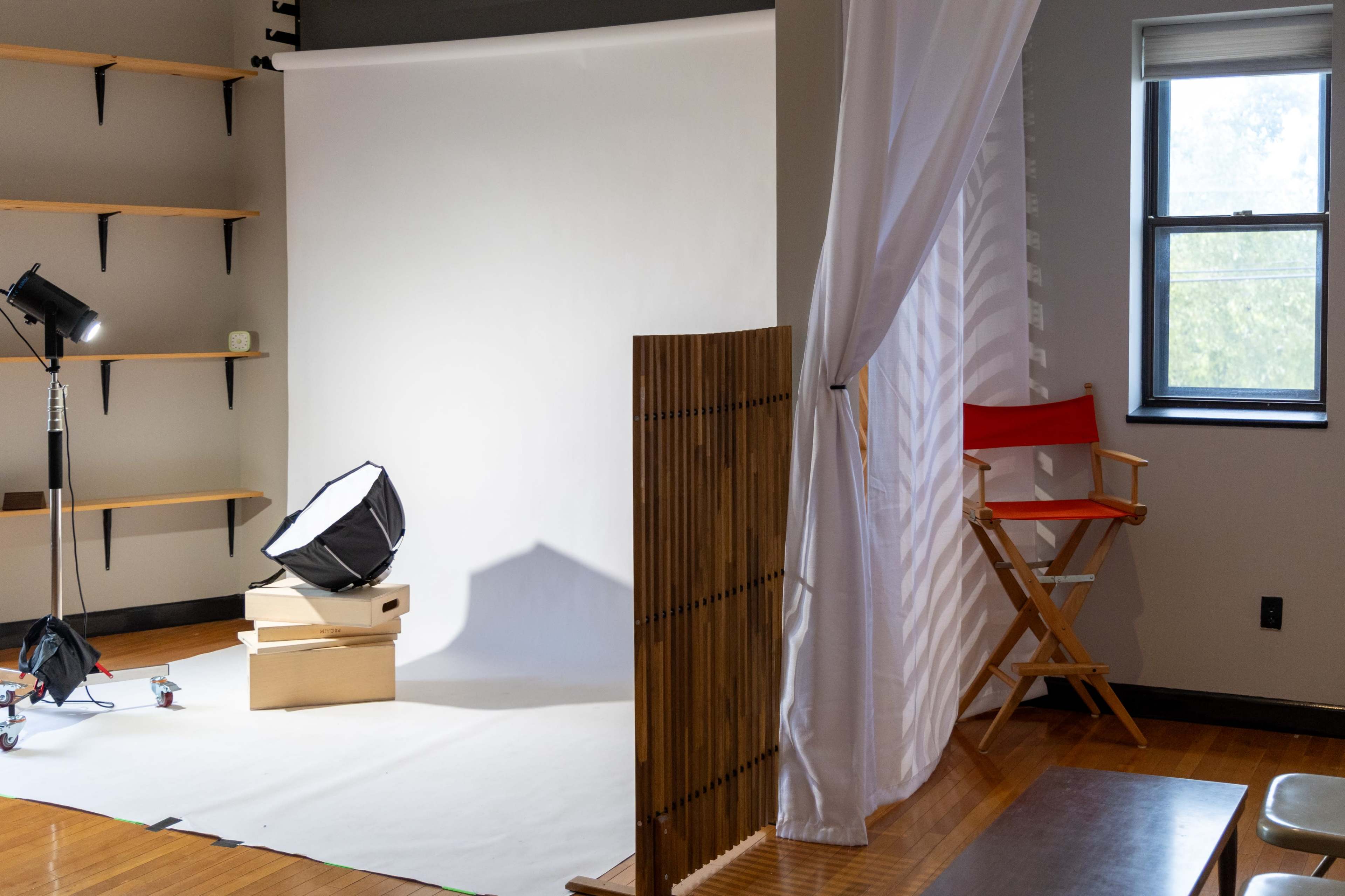 The image shows a photography studio setup with a backdrop, lighting equipment, and a director's chair beside a curtain.