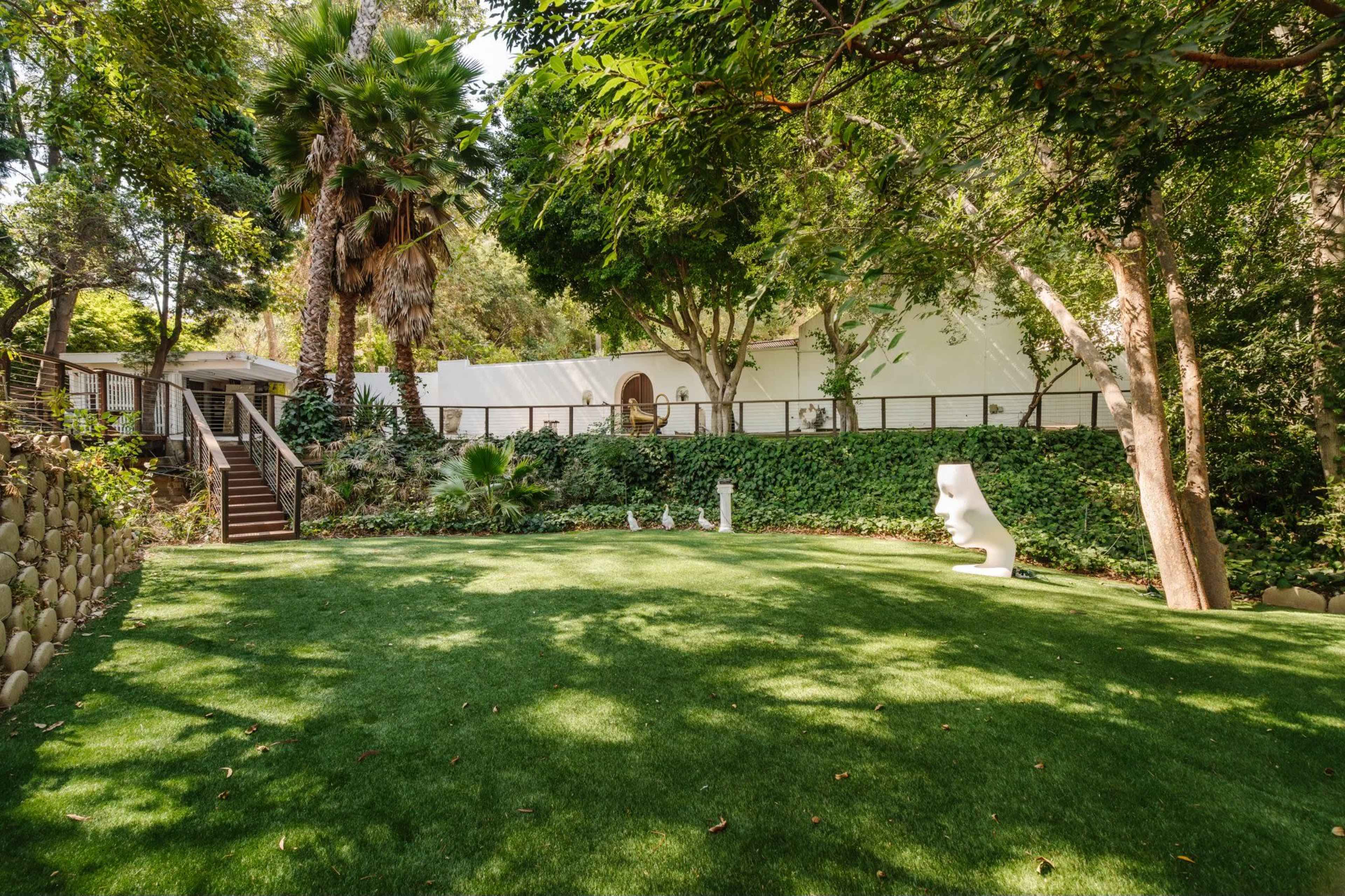 The image shows a spacious, landscaped backyard featuring a manicured lawn, decorative sculptures, and lush trees.