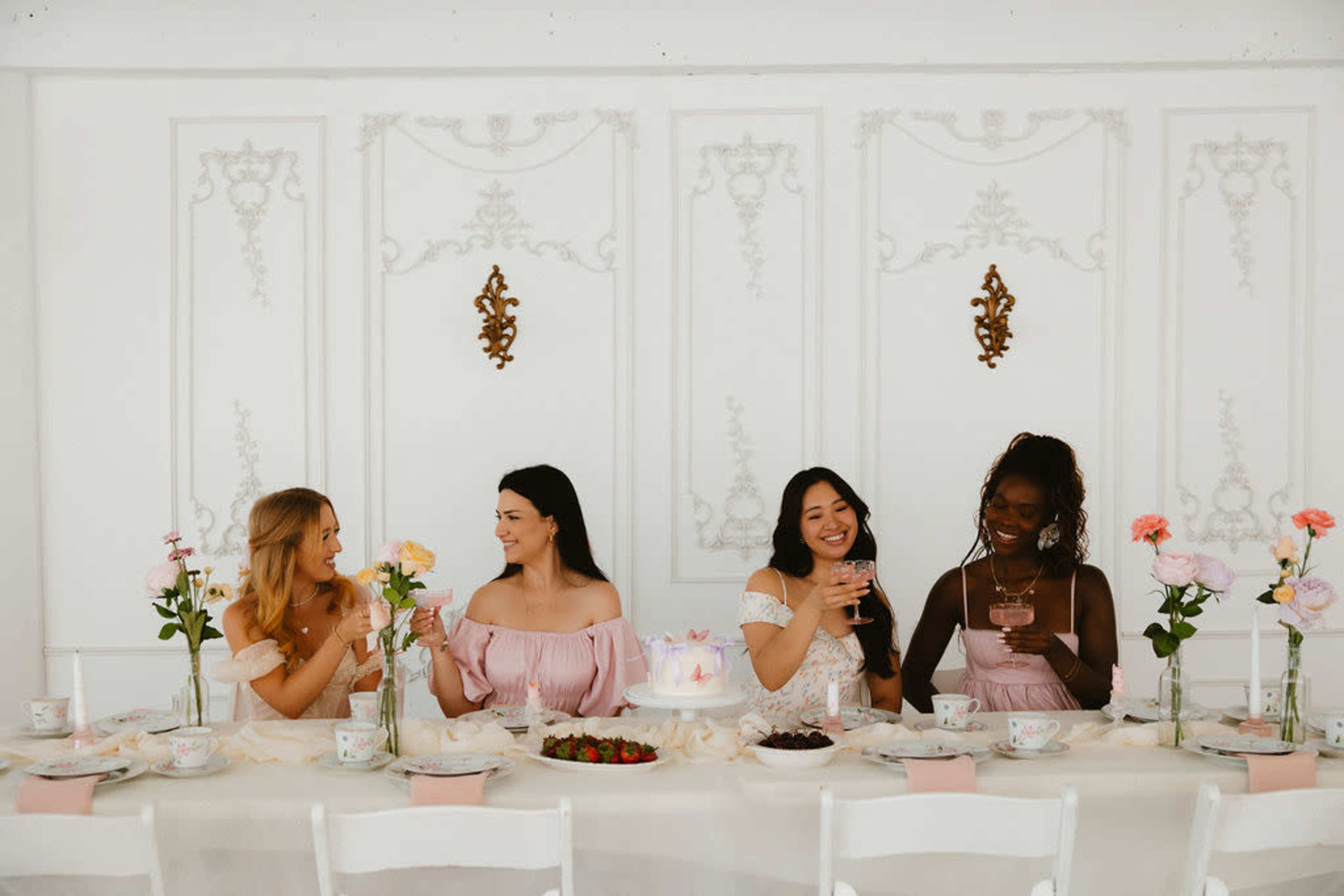Four women sit at a elegantly set table adorned with flowers, enjoying drinks and dessert.