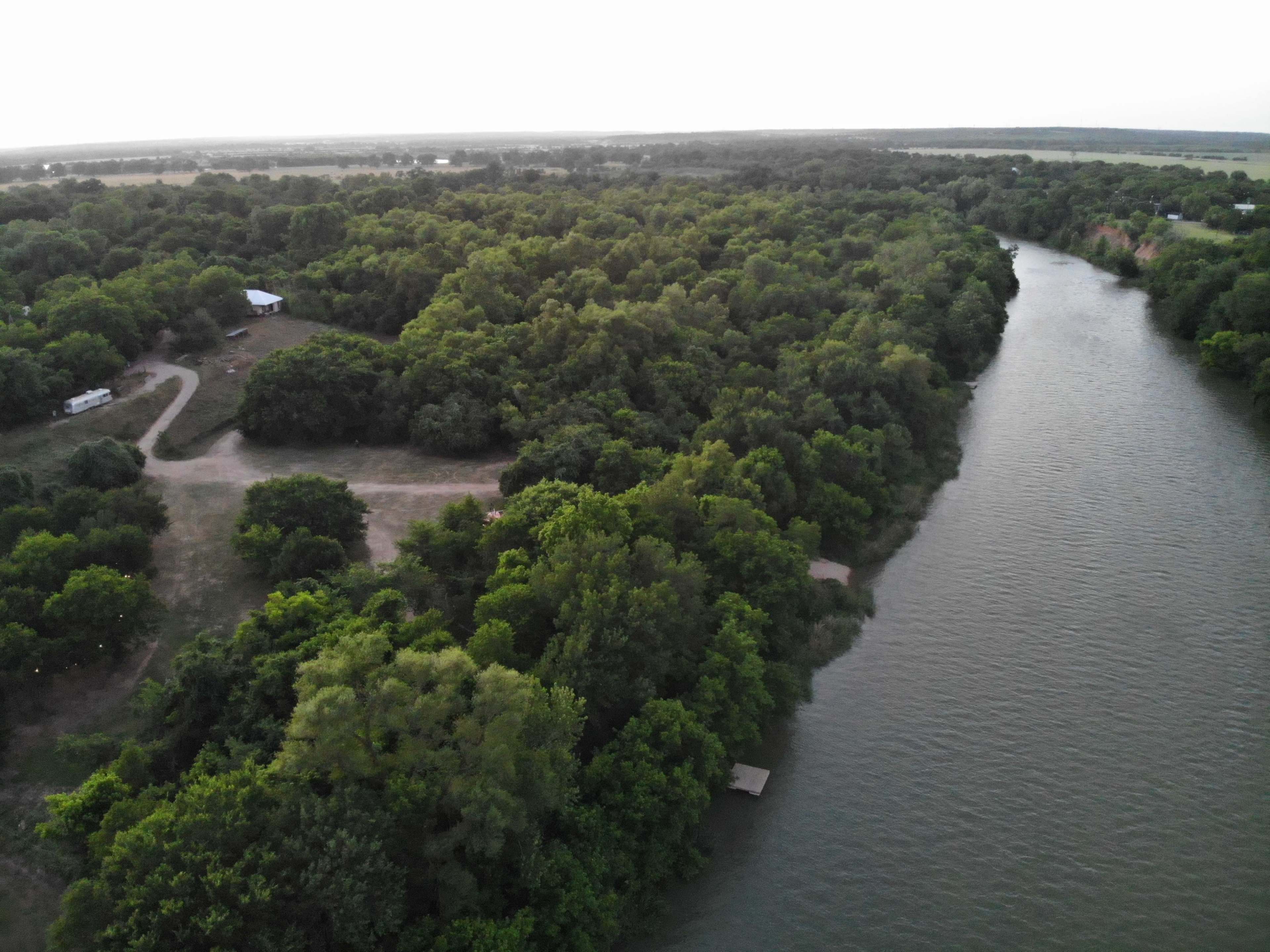 A winding river bordered by dense green vegetation and scattered structures in the background.