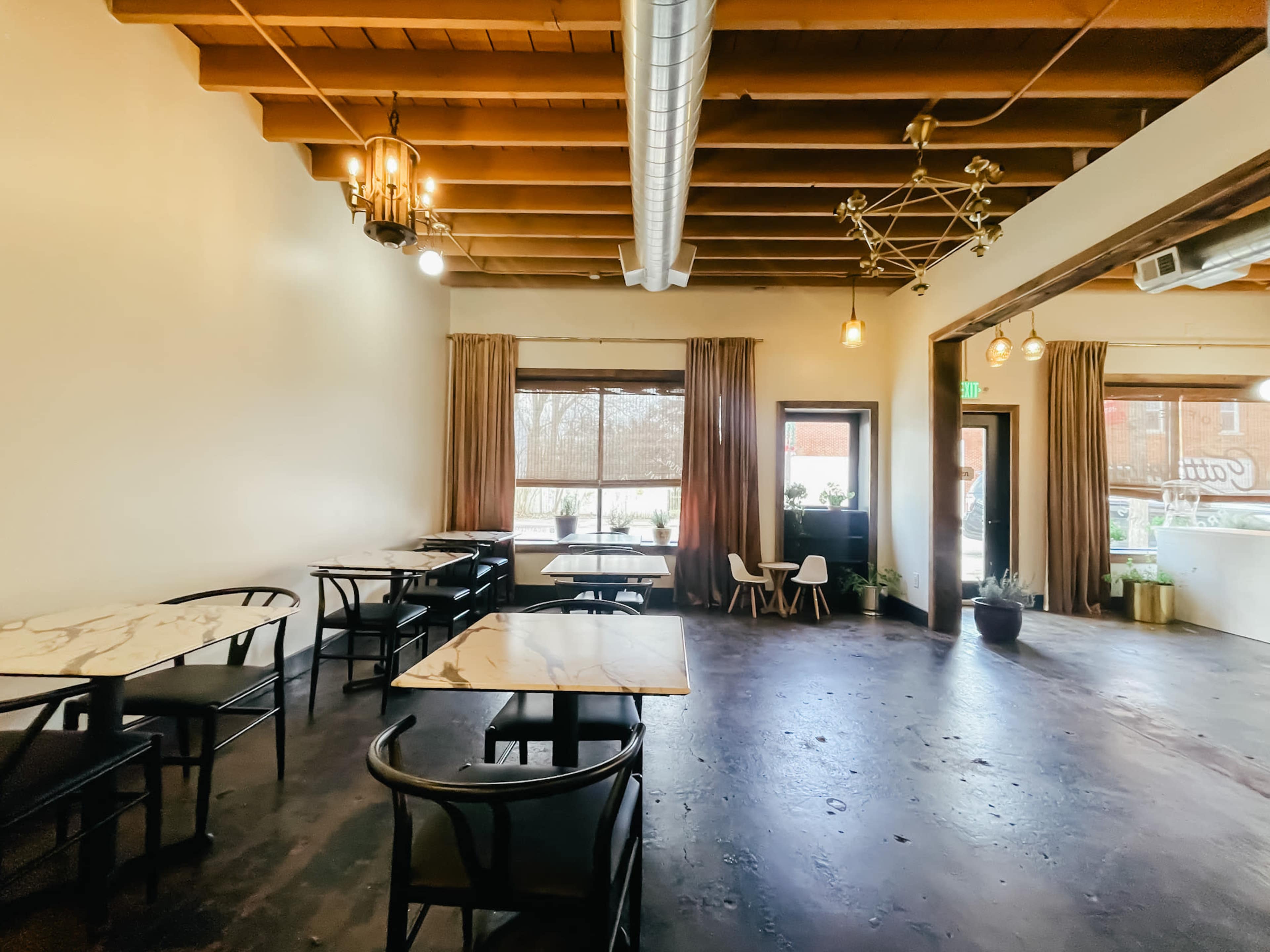 The image shows a spacious café interior featuring marble-topped tables, wooden beams, and large windows with natural light.