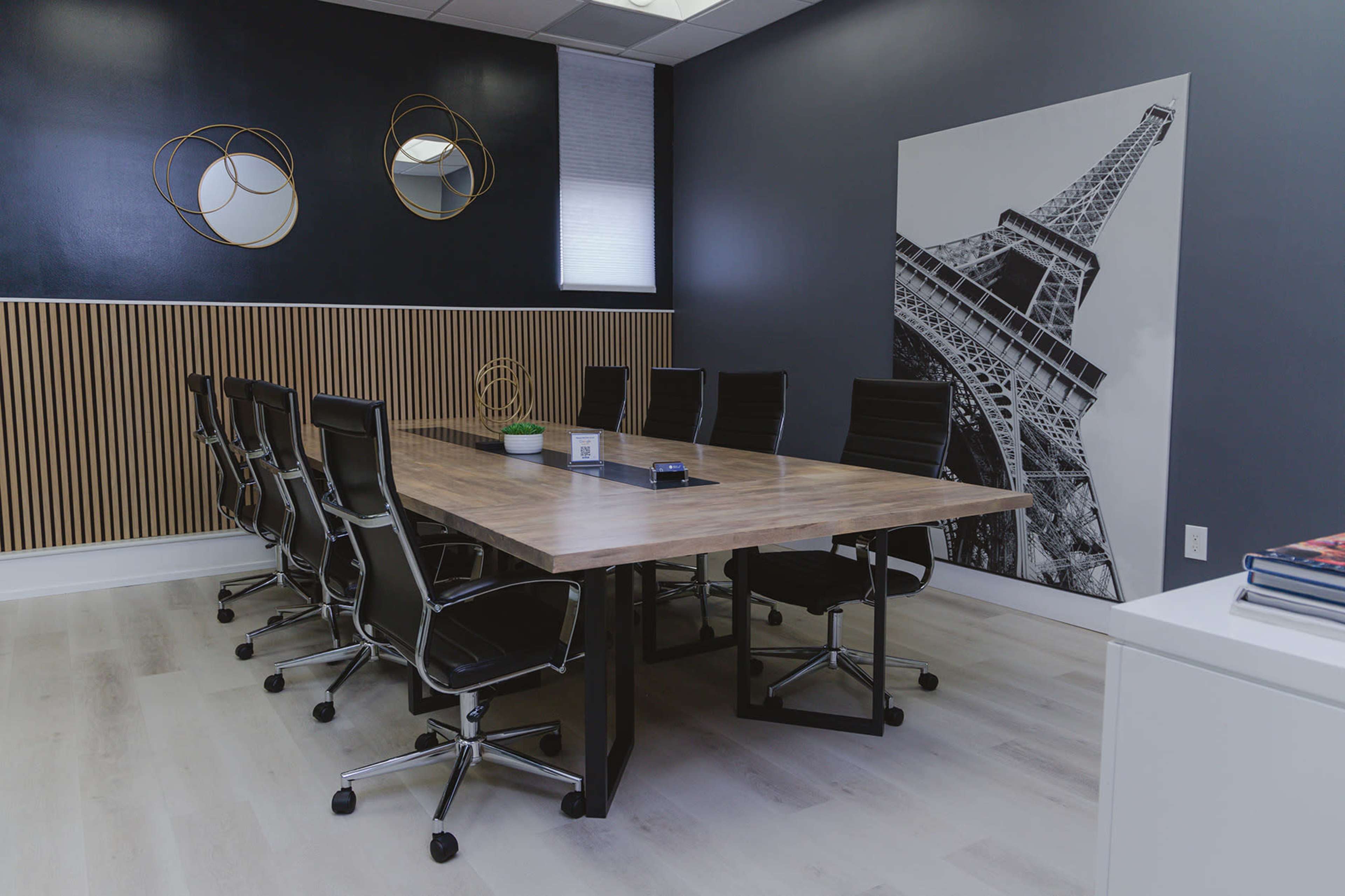 A modern conference room features a long wooden table surrounded by black ergonomic chairs, with a large black-and-white photograph of the Eiffel Tower on one wall.