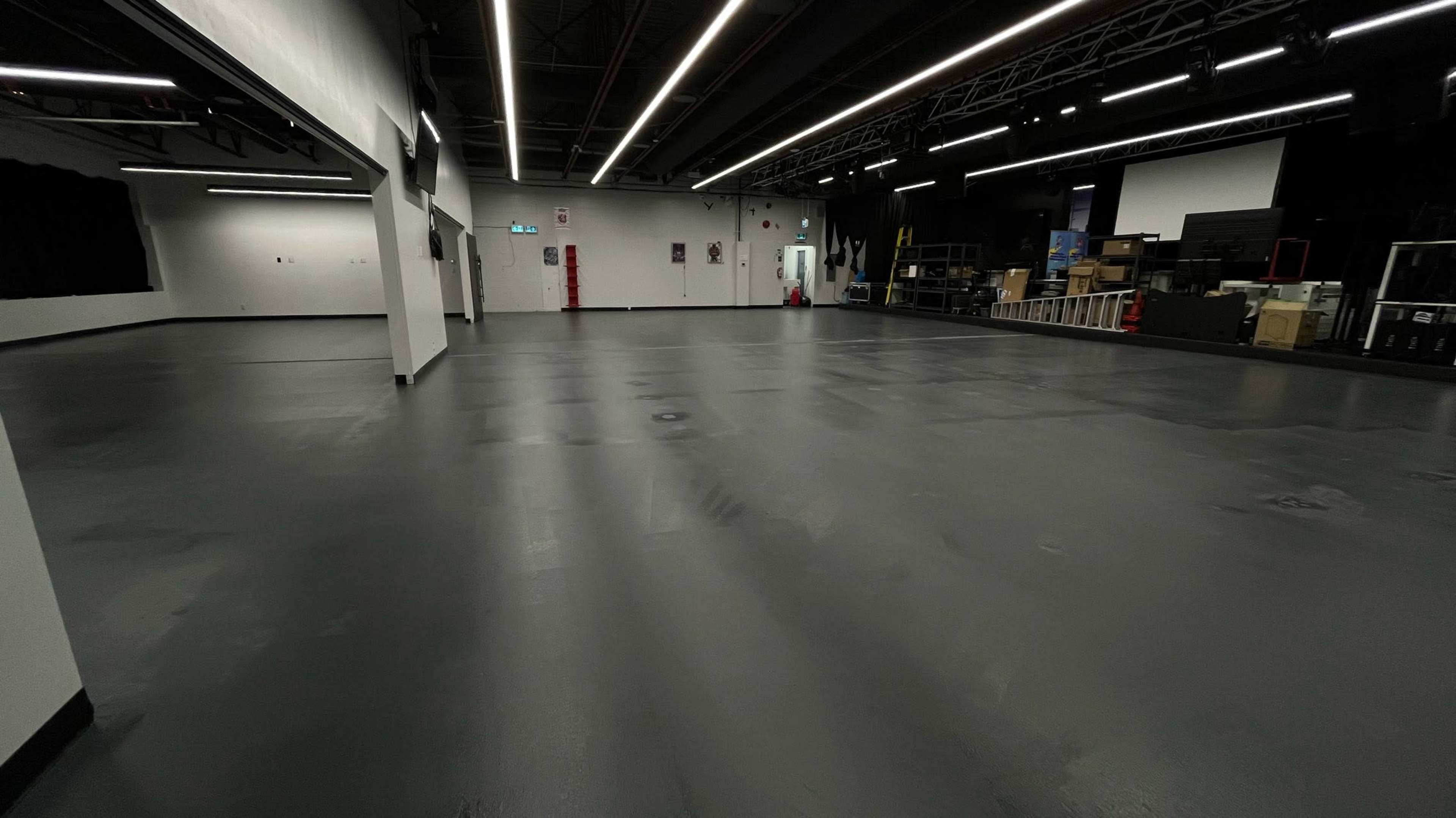 A large, empty indoor space with a smooth, dark floor and various equipment stored along the walls.