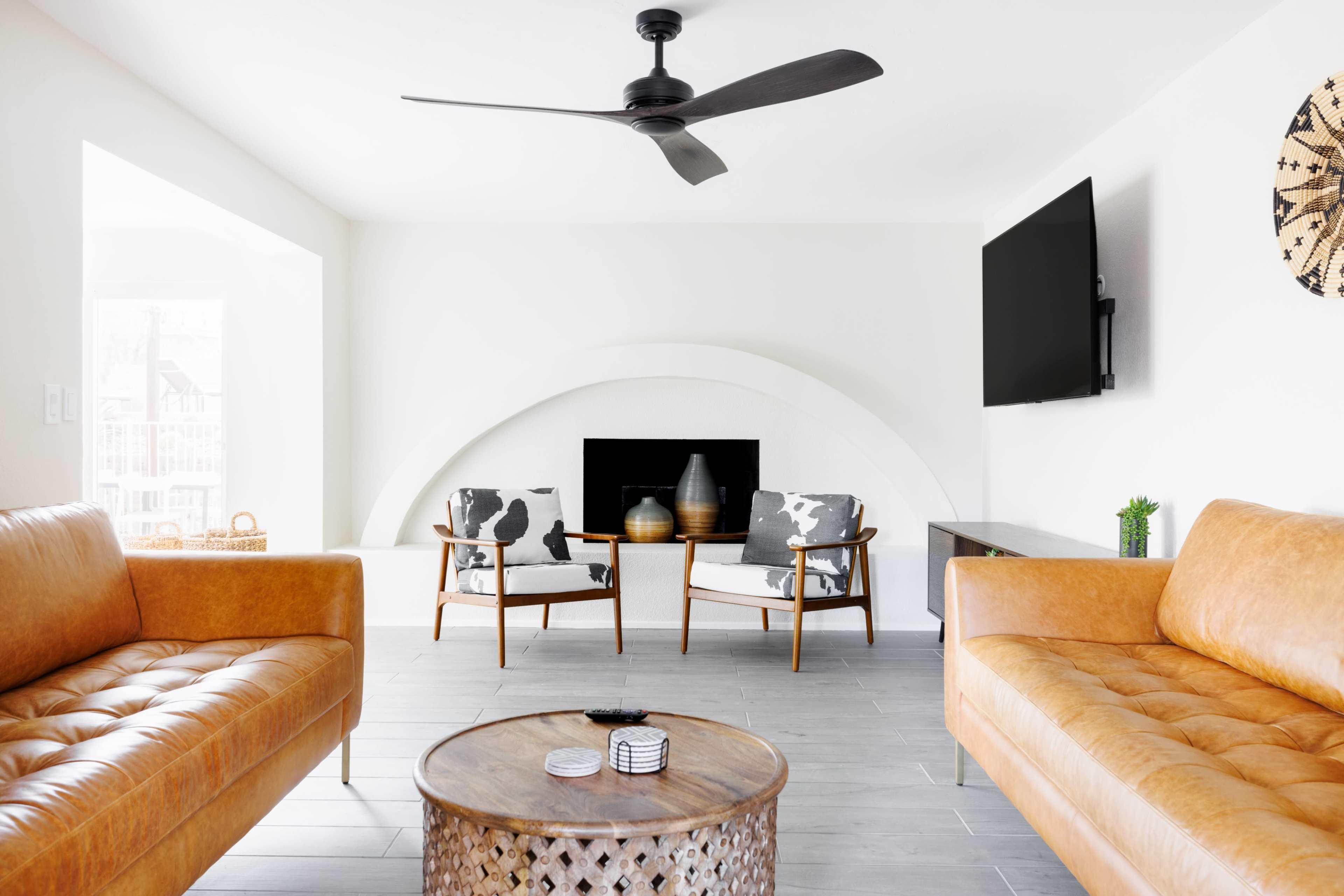 A modern living room featuring two leather sofas, a wooden coffee table, and a fireplace with two chairs positioned nearby.