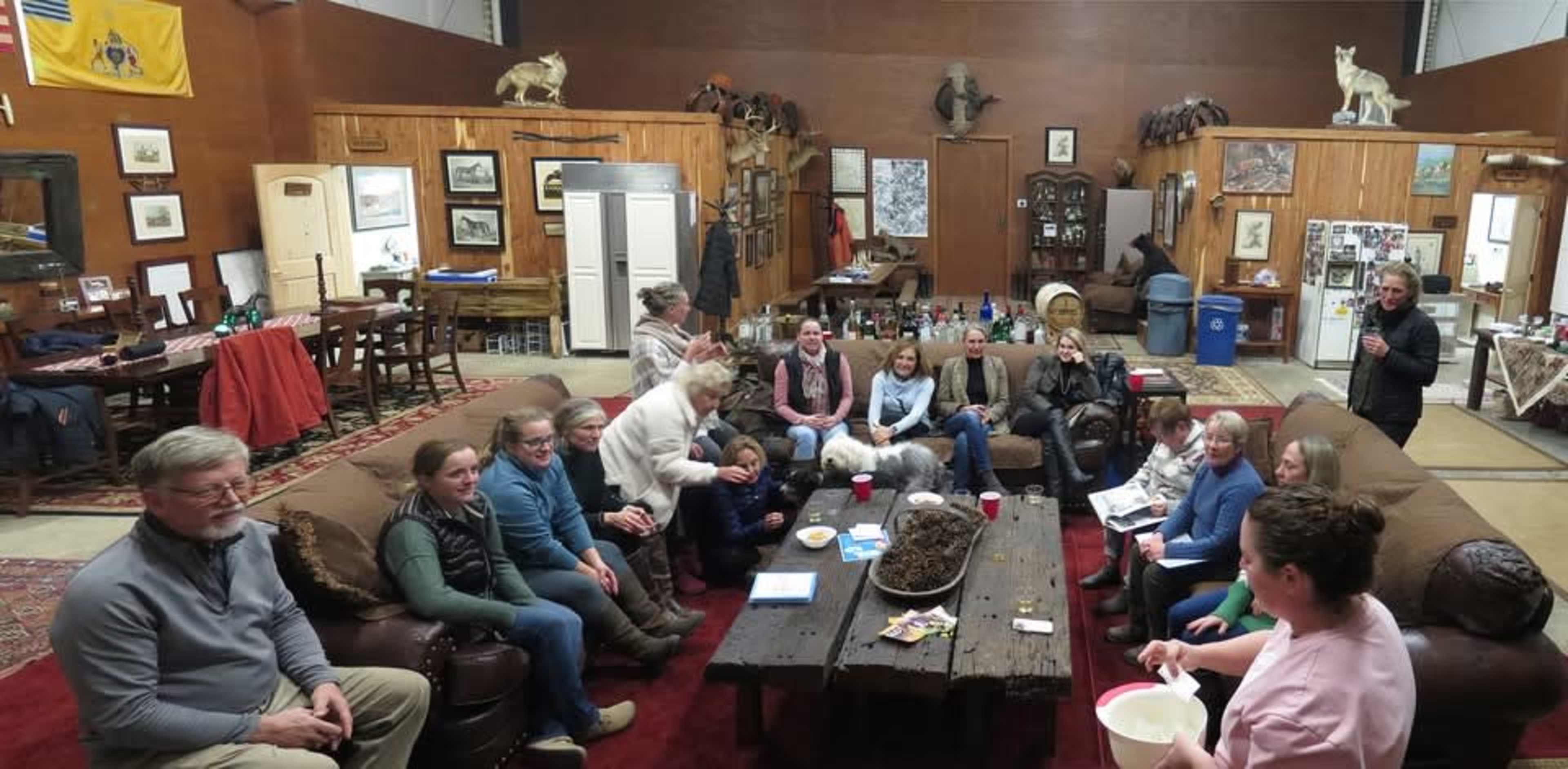 A group of people sits on sofas in a large room filled with rustic decor and various recreational items.