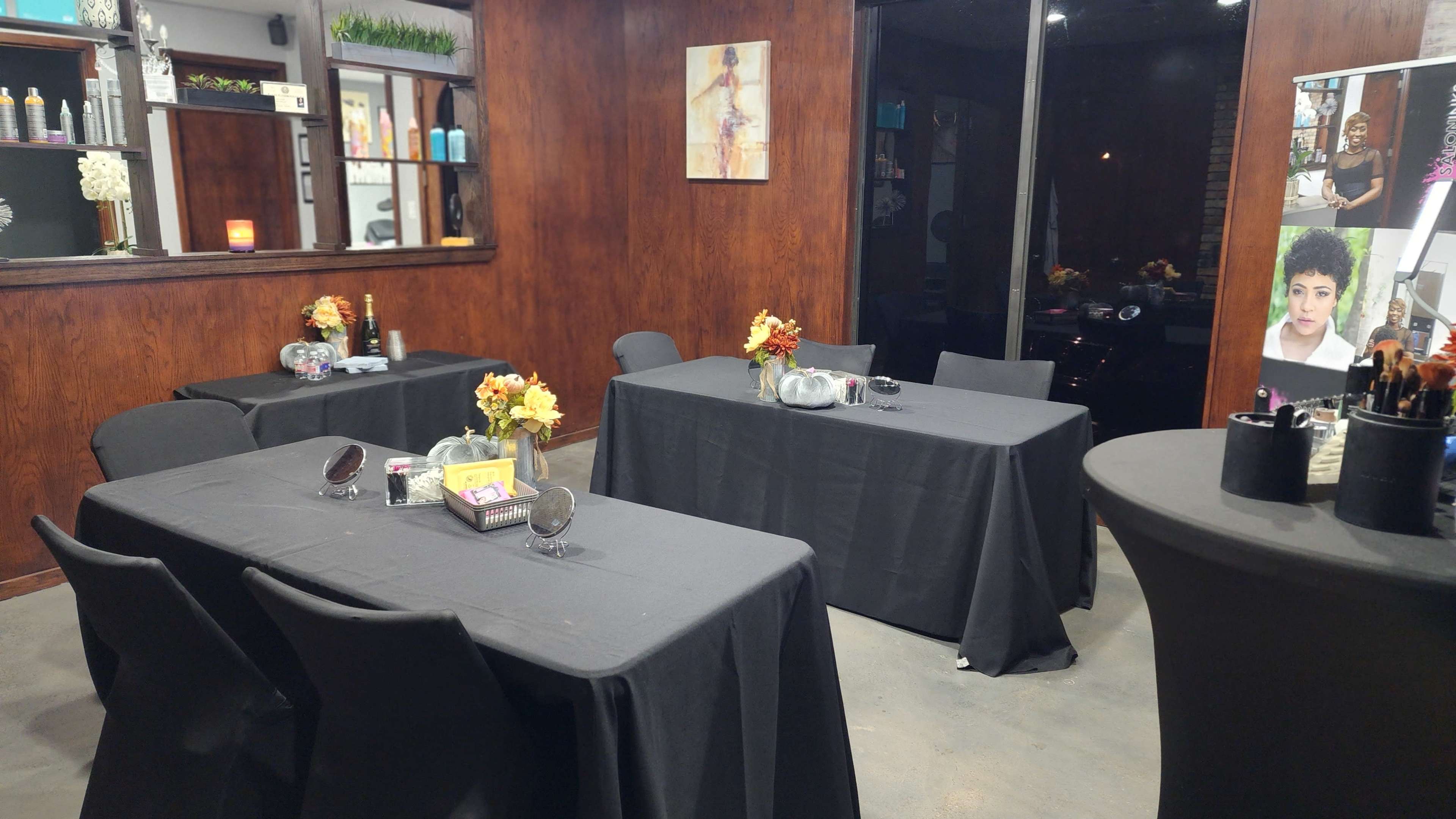 The image shows a dimly lit salon room with several covered tables decorated with vases of flowers and mirrors.
