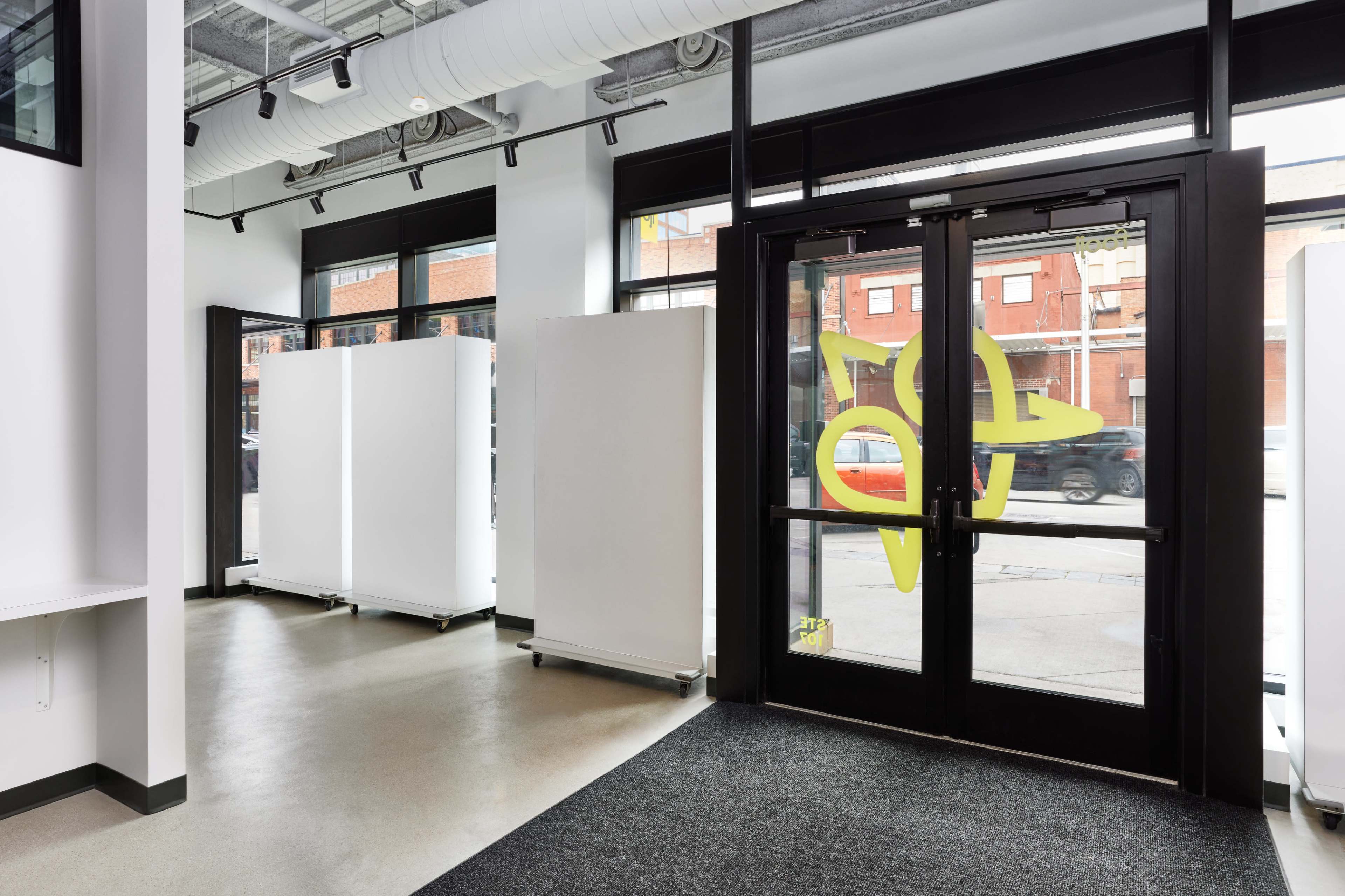 The entrance of a modern commercial space featuring glass doors and minimalist white displays on wheels.