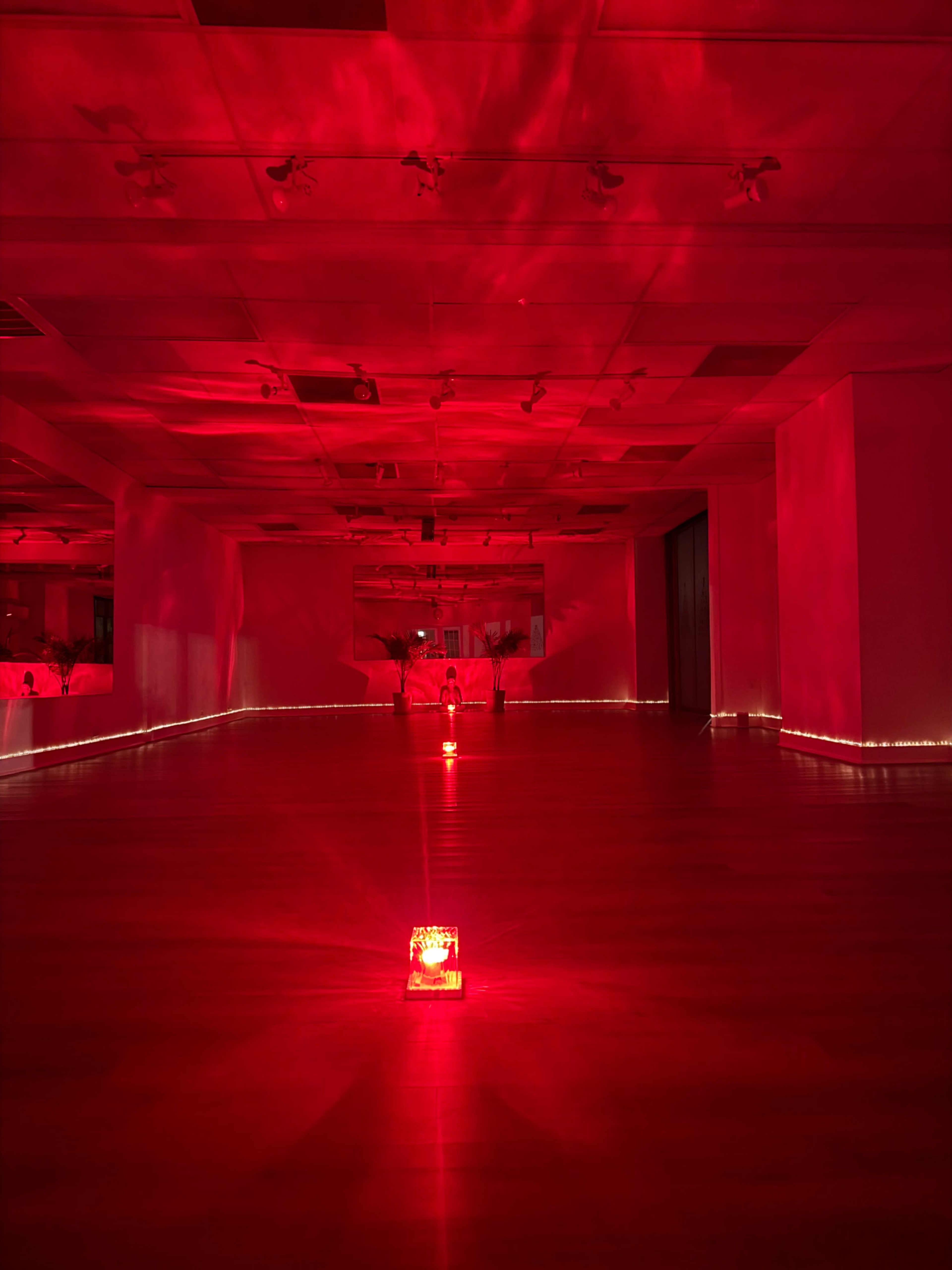 The image shows a spacious room illuminated primarily in red light, featuring several red light sources on the floor and a reflective surface.