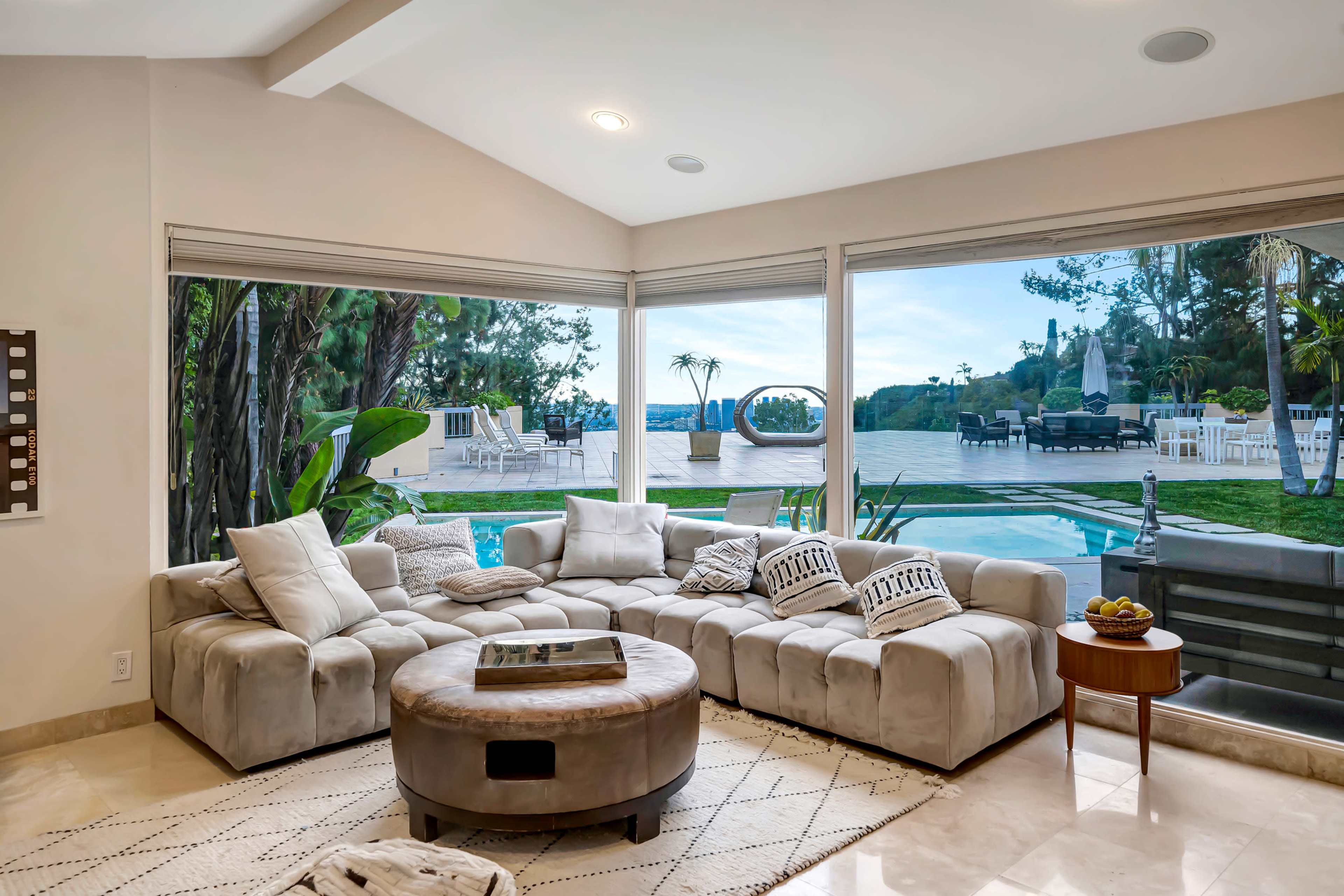 A spacious living room features a large sectional sofa facing expansive windows that offer a view of a pool and outdoor seating area.