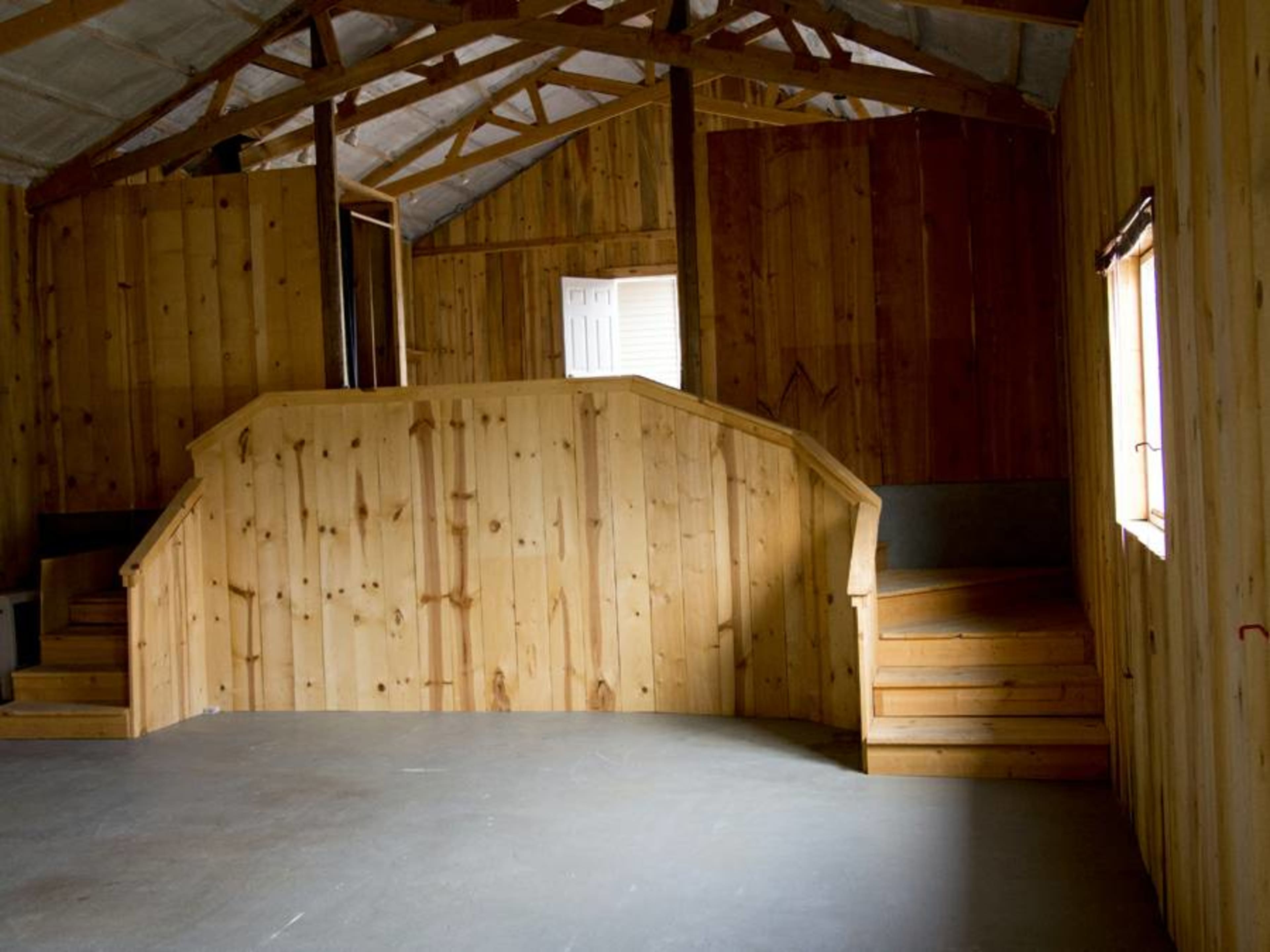 The interior of a wooden building features a spacious, unfinished area with wooden stairs leading to a raised platform.