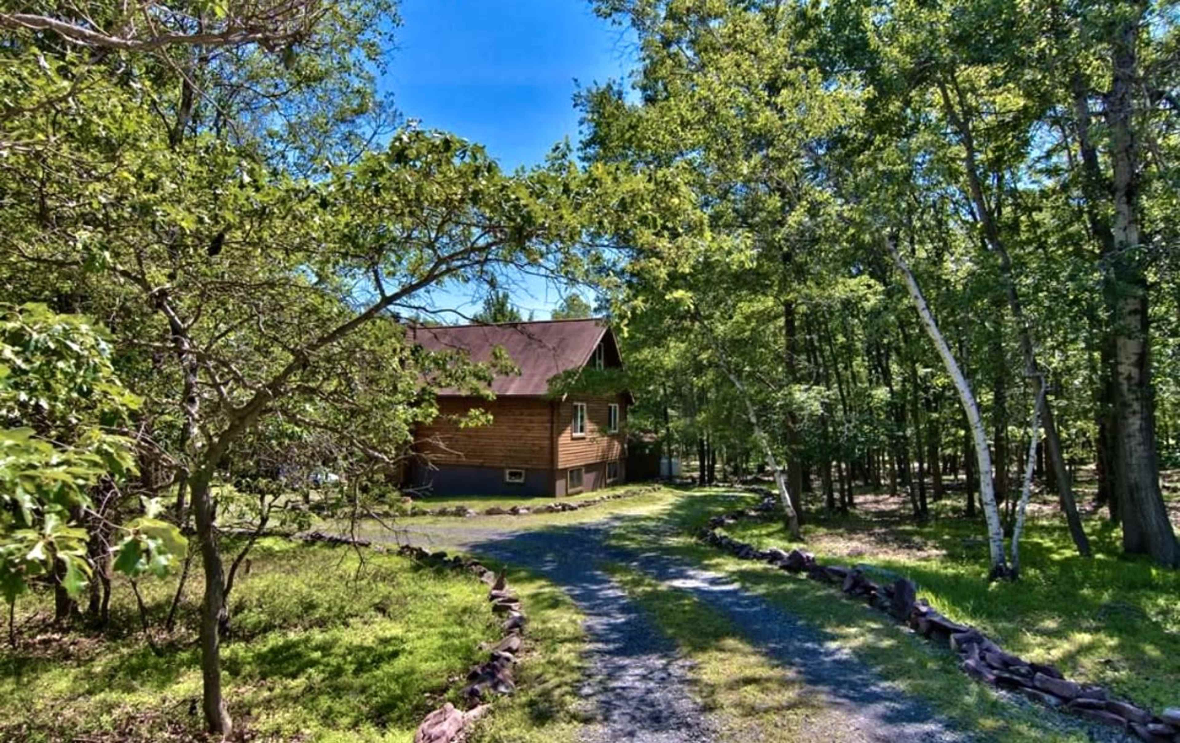 A wooden cabin is situated along a gravel pathway surrounded by trees in a wooded area.