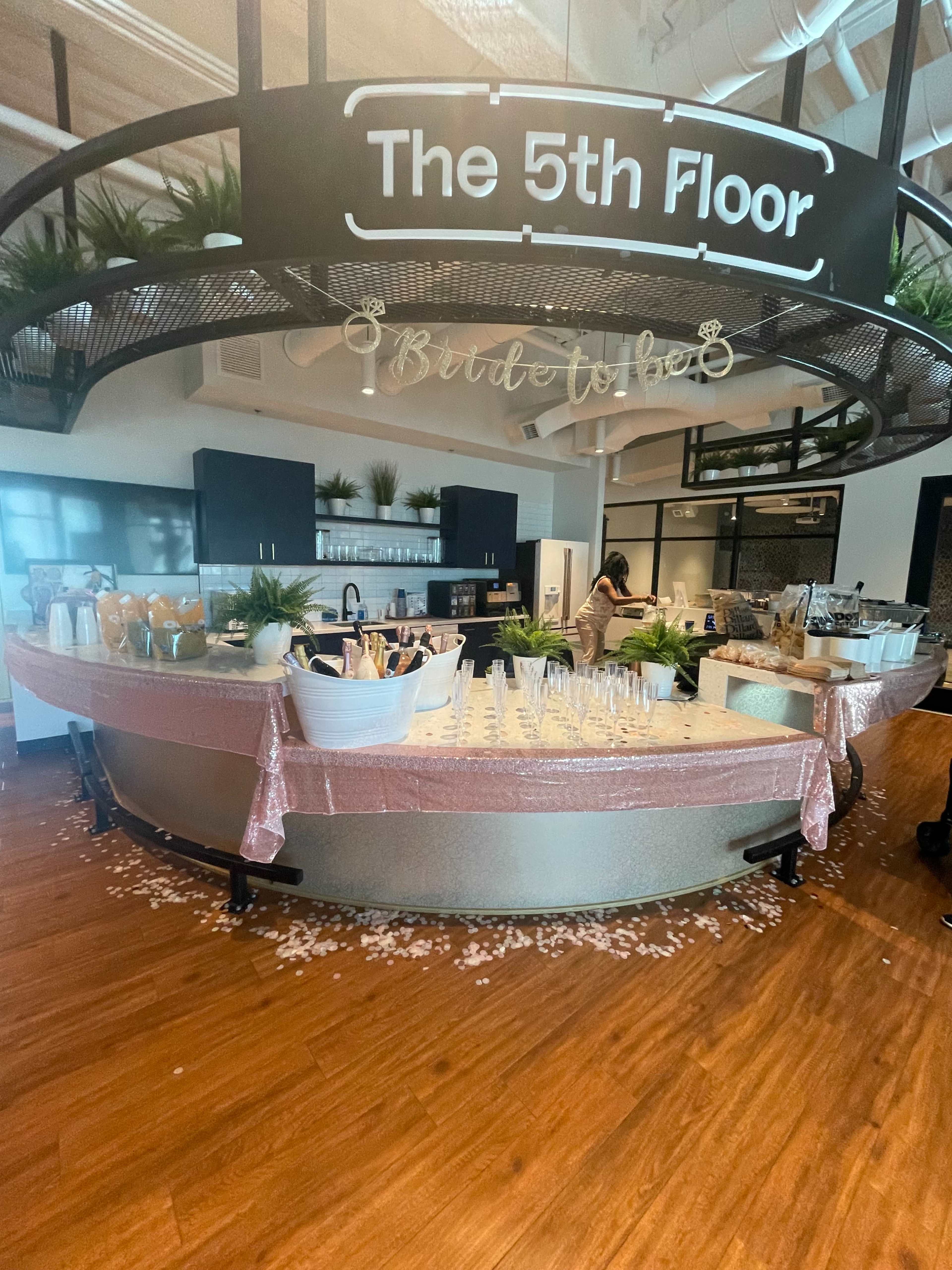 A modern event space featuring a circular bar setup adorned with decorative elements and a variety of glassware, set against stylish kitchen facilities.