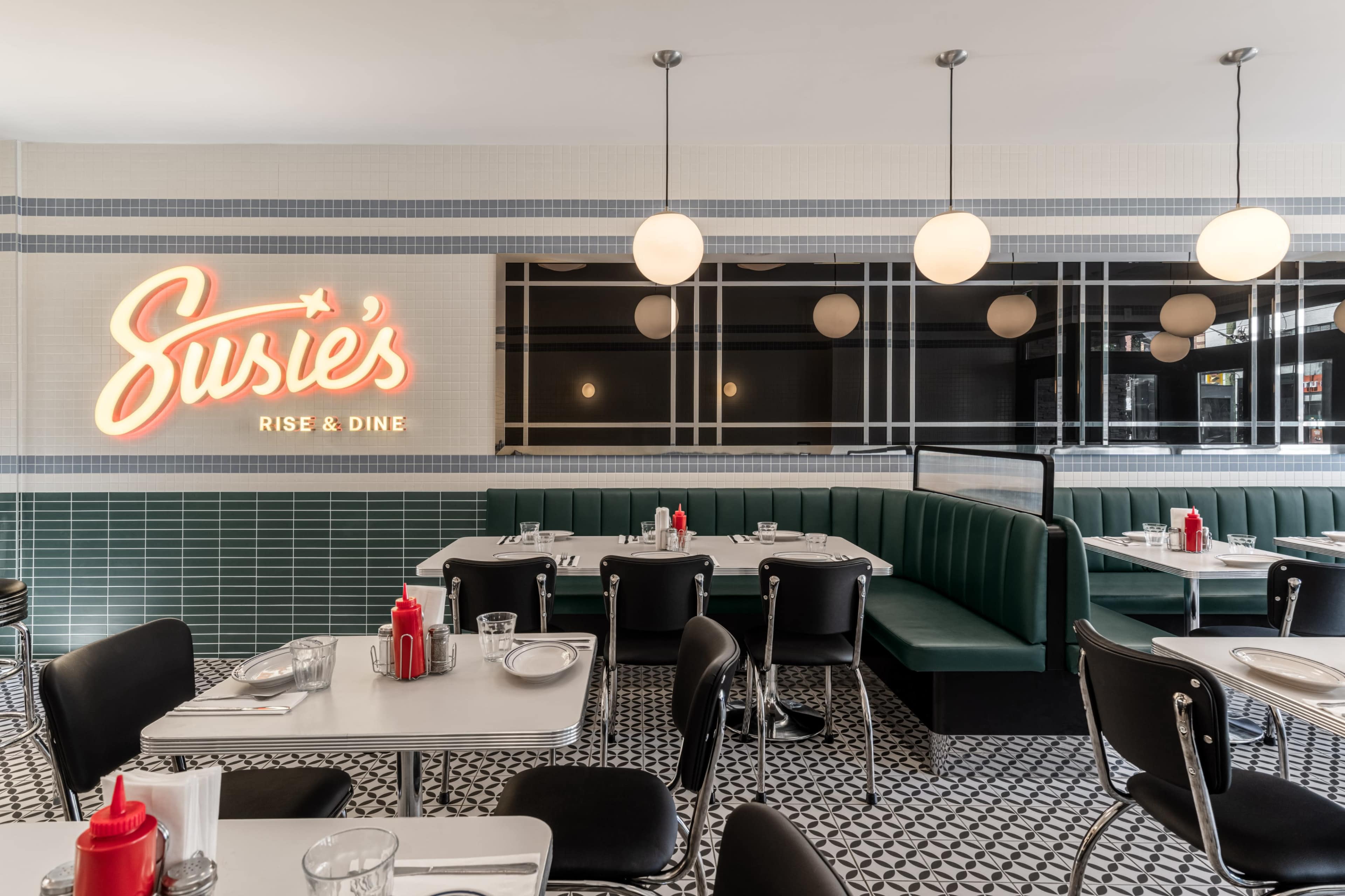 The image shows a retro-style diner with green booth seating, white tables, and a neon sign reading "Susie's Rise & Dine" on the wall.