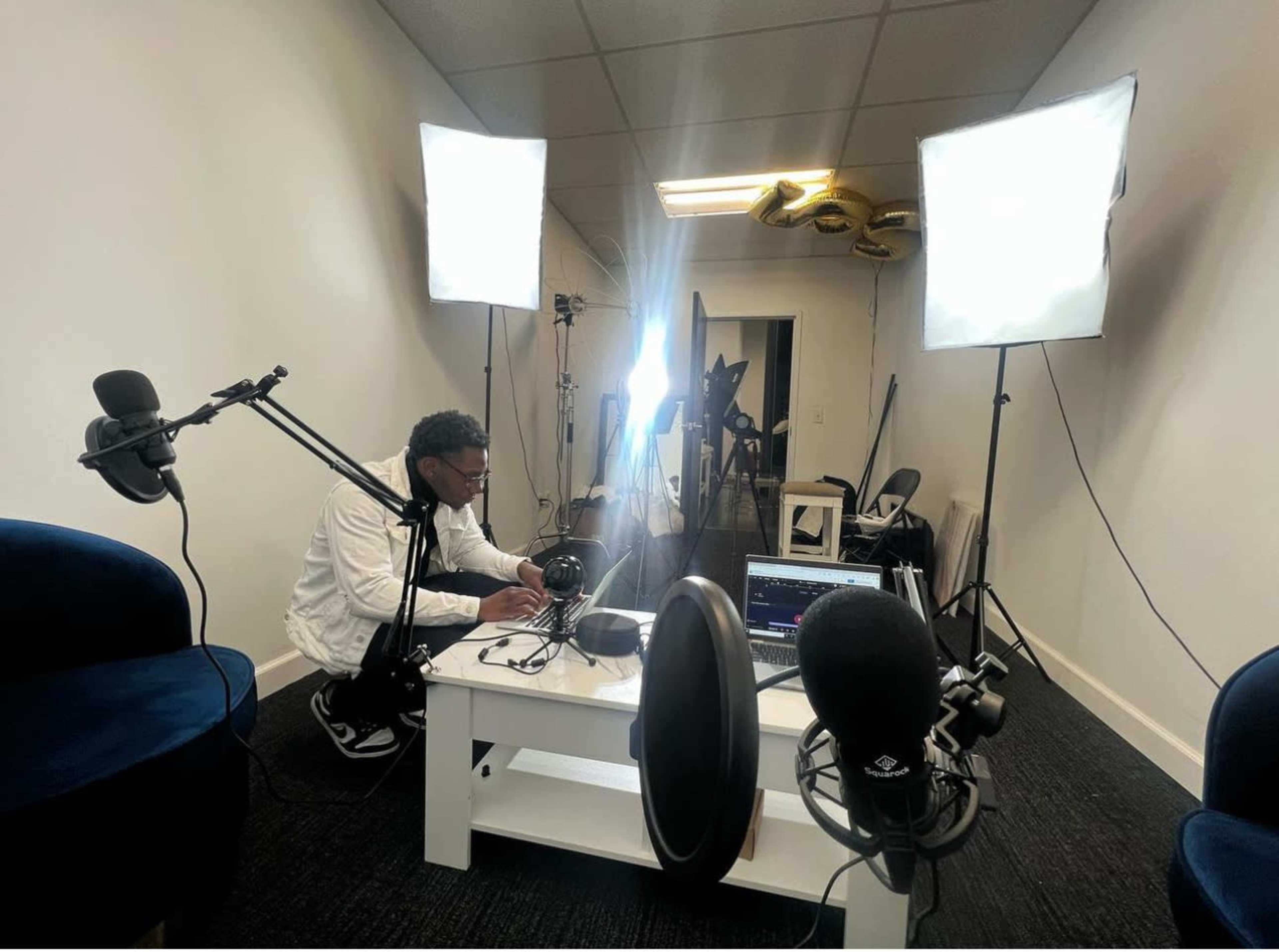 A person is setting up audio equipment in a well-lit recording studio with multiple softbox lights and microphones.