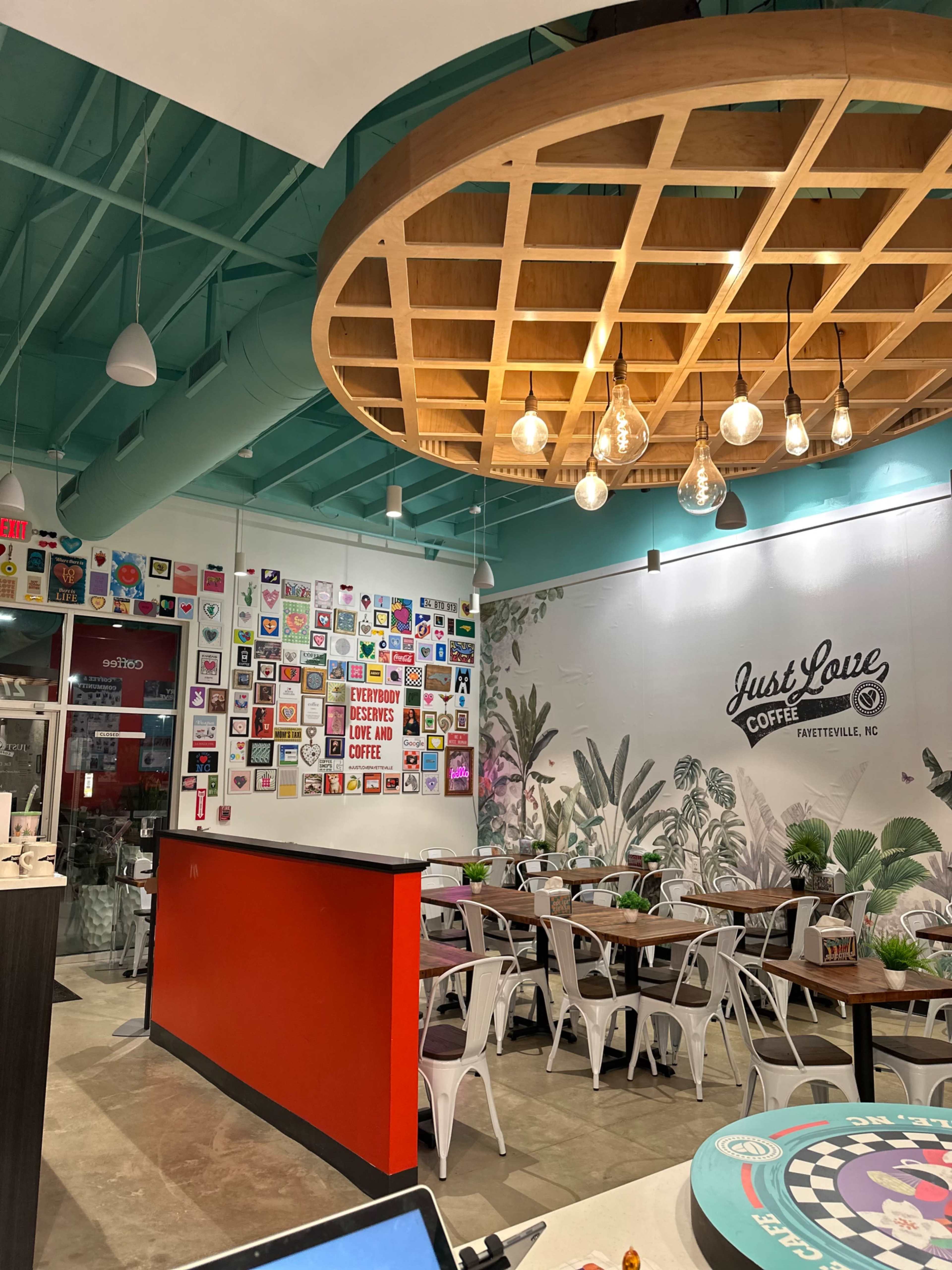A modern coffee shop interior with a wooden ceiling, a feature wall adorned with various artworks, and tables arranged for seating.