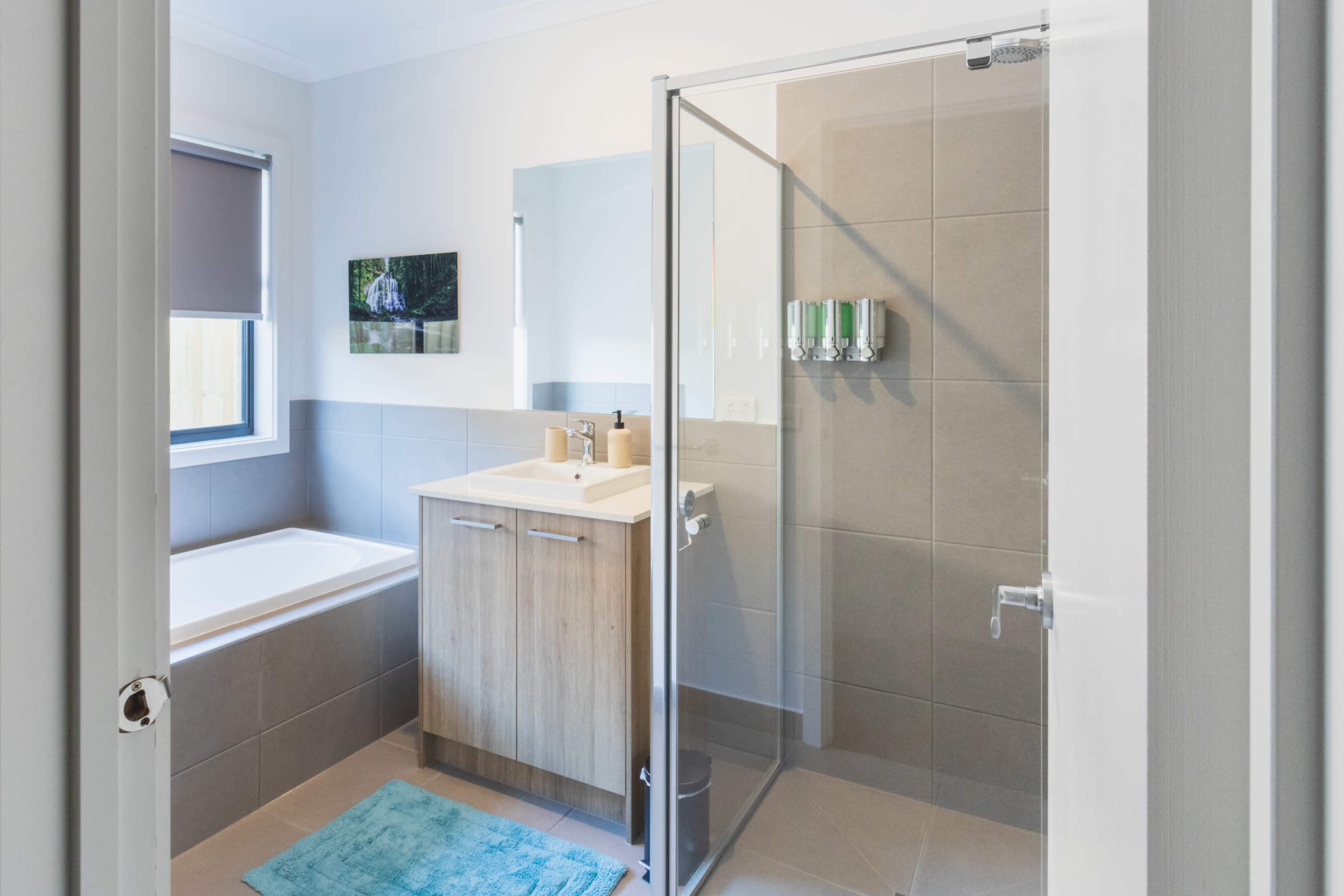 A modern bathroom features a glass shower enclosure, a bathtub, and a wooden vanity with toiletries, illuminated by natural light from a window.