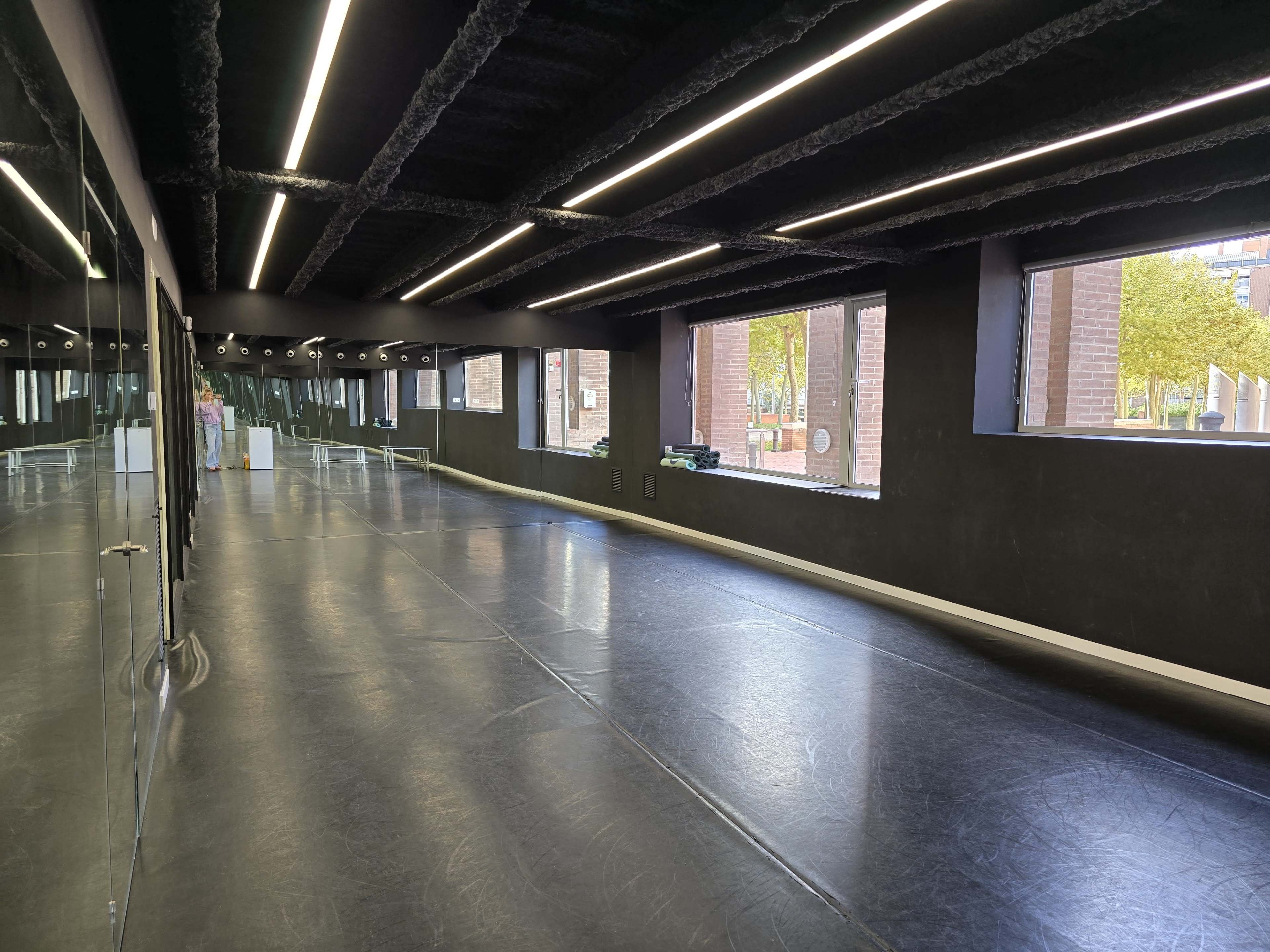The image shows a spacious, modern dance studio with large windows, black walls, and a glossy floor.