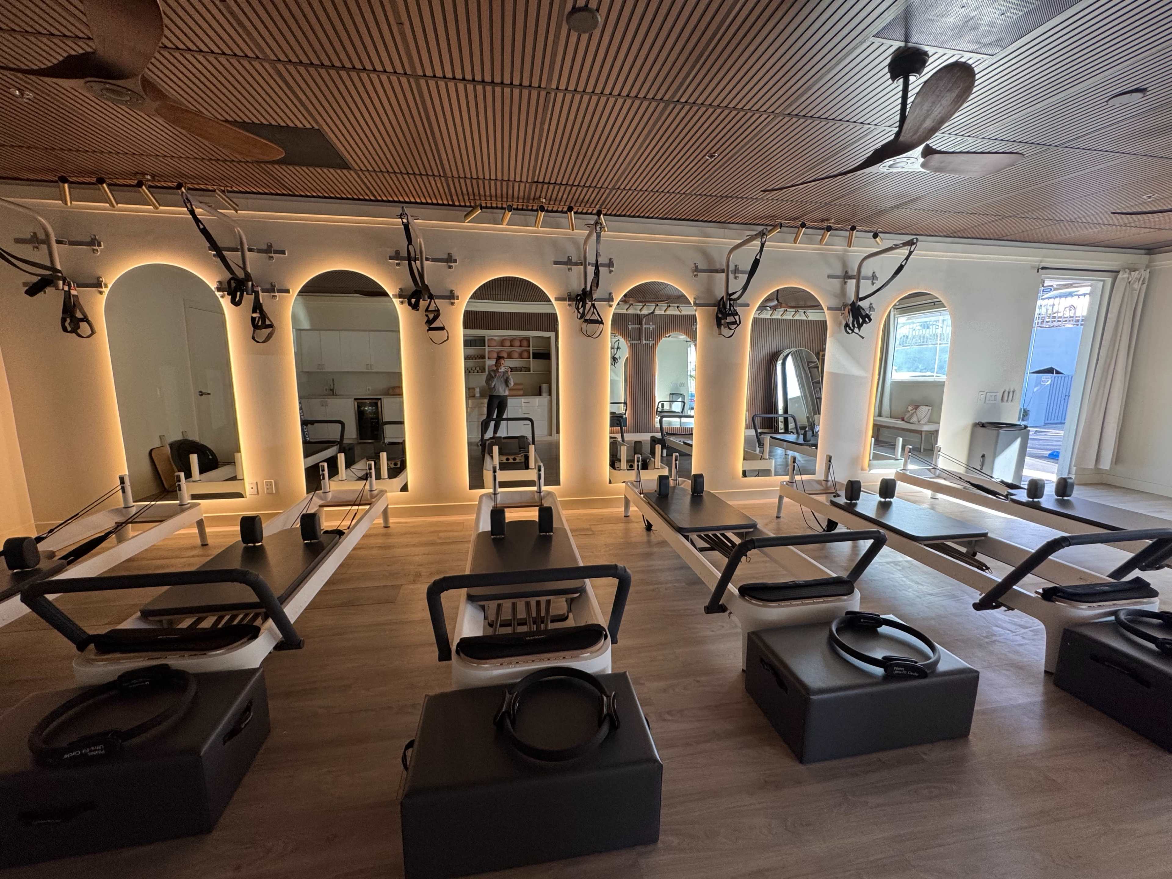 The image shows a modern fitness studio equipped with multiple reformer Pilates machines arranged in rows under soft lighting.