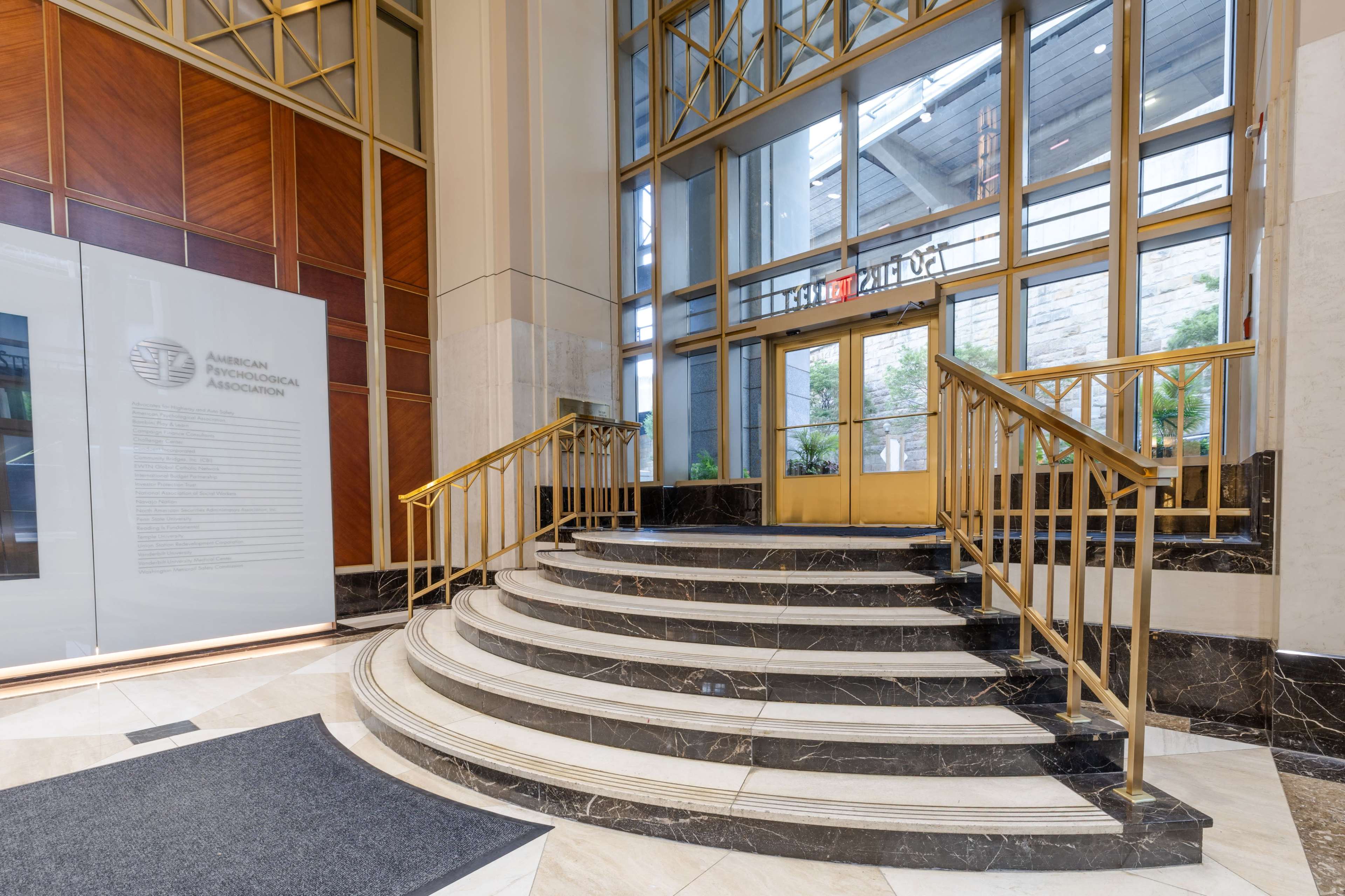 The image shows a grand entrance with a curved marble staircase leading to a set of glass doors.