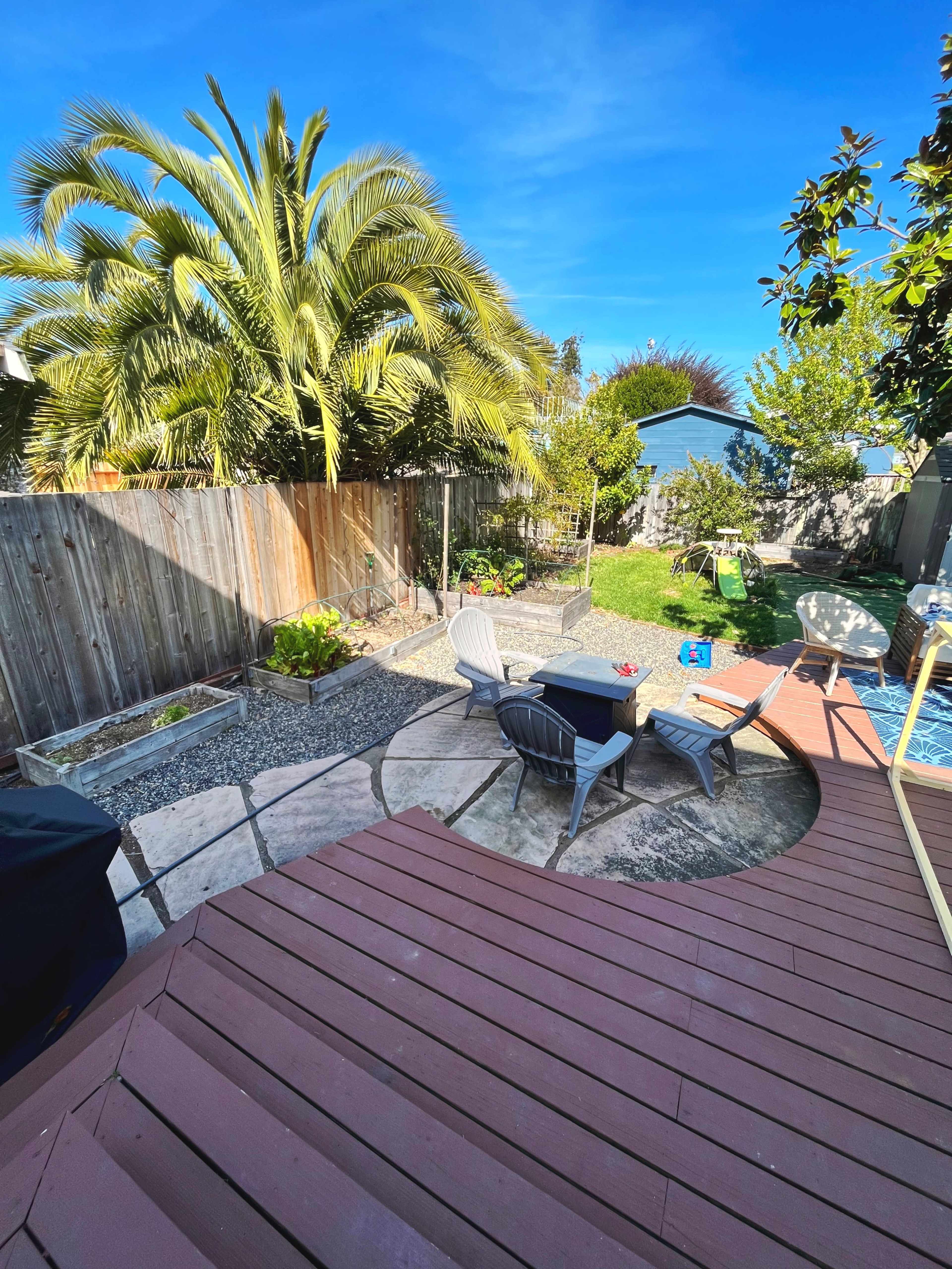 A backyard scene features a patio area with chairs, greenery, and a swimming pool under a clear blue sky.