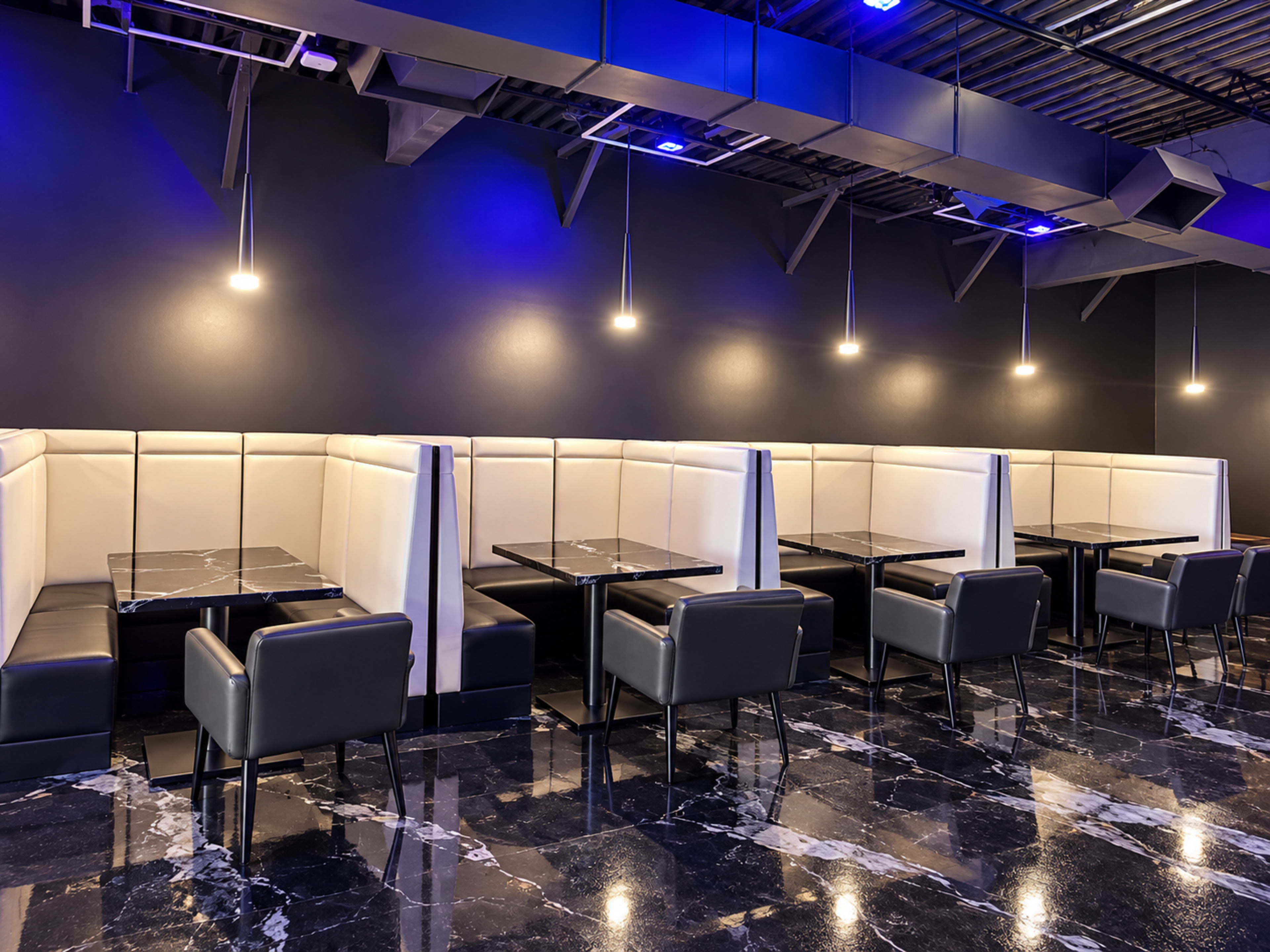 The image shows a modern restaurant interior featuring black marble flooring, white and black cushioned booths, and dim lighting from overhead fixtures.