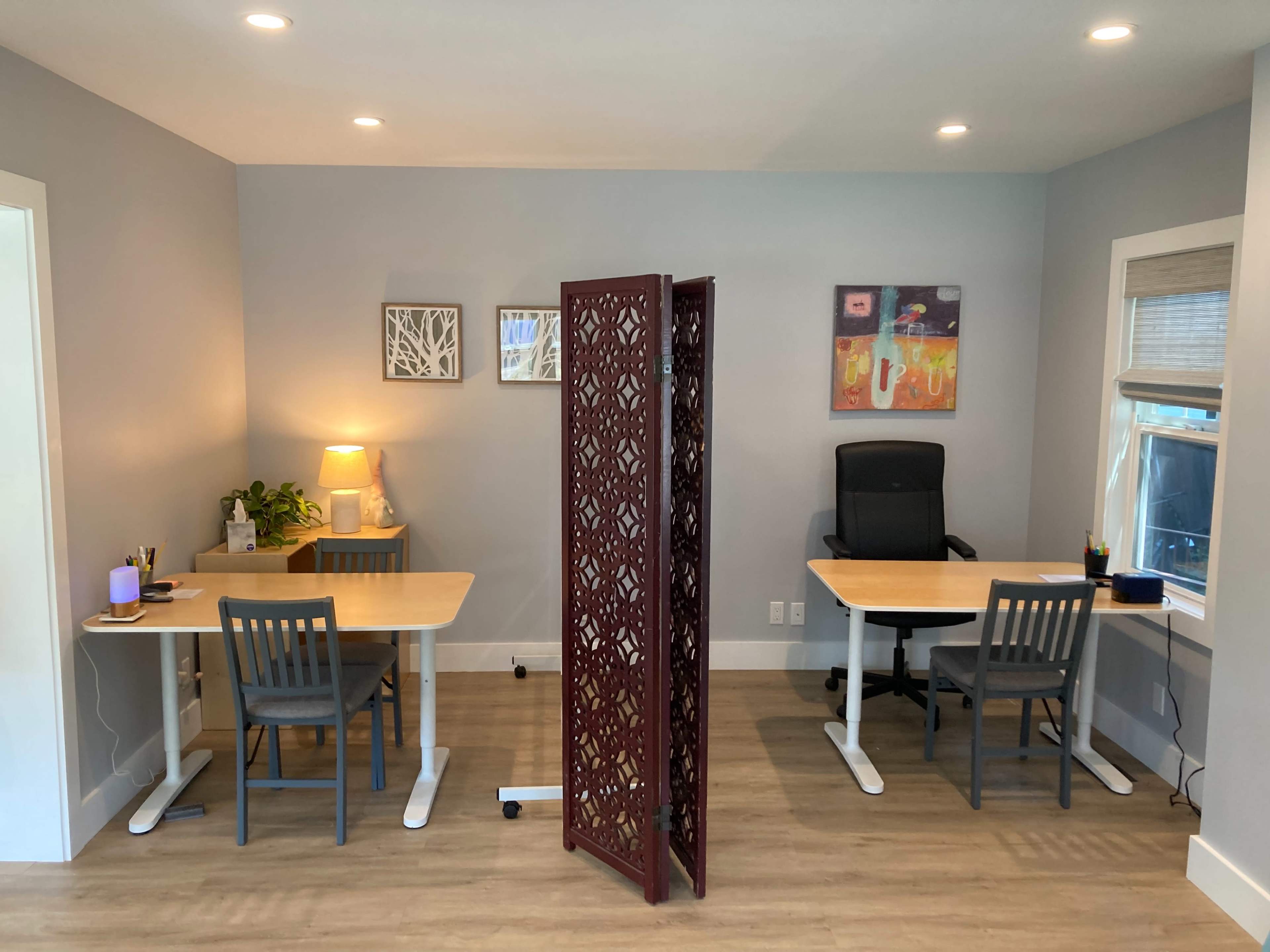 A modern office space with two workstations separated by a decorative screen, one side featuring a lamp and plant, and the other side with a chair and desk.