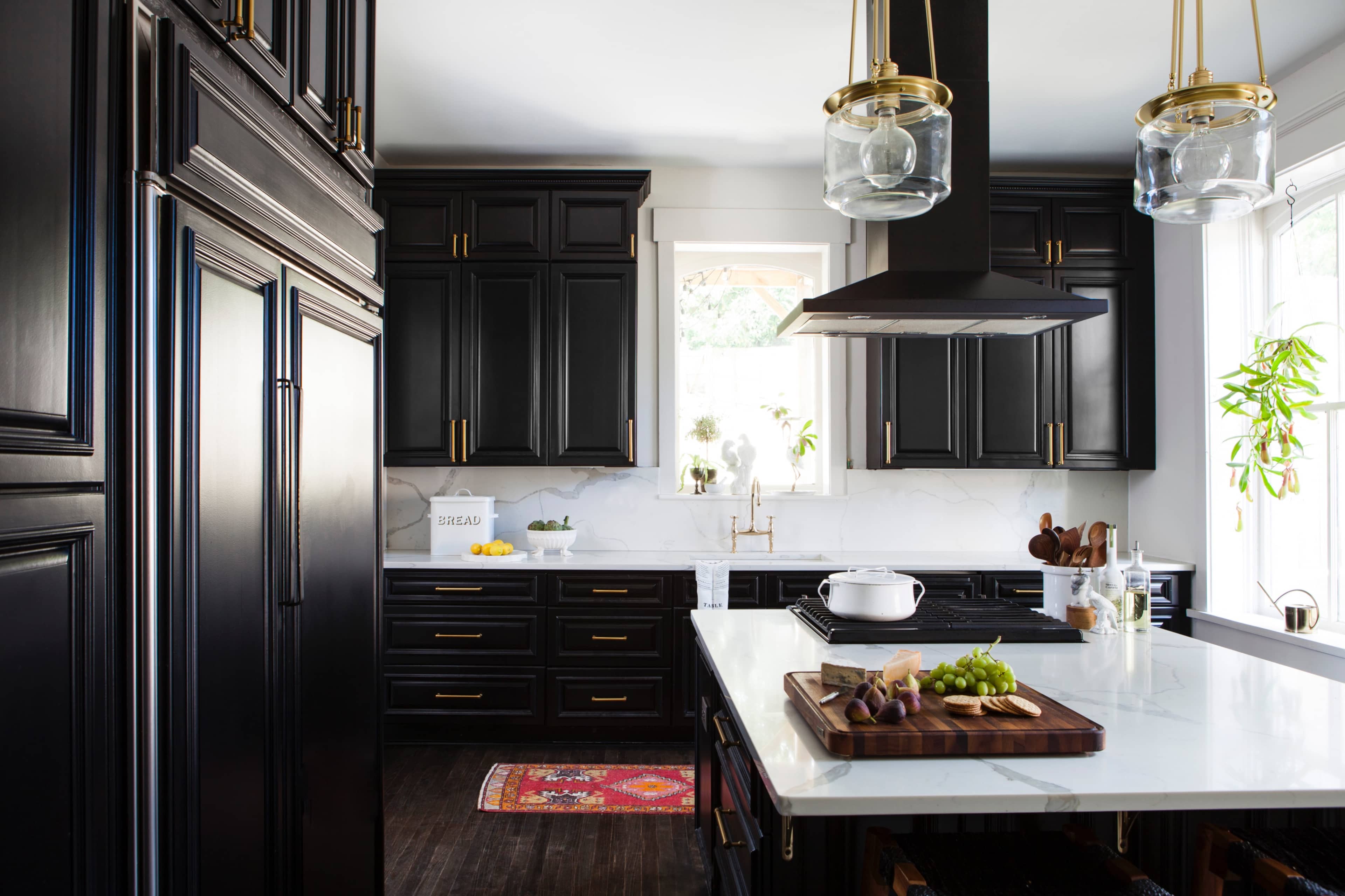 A modern kitchen with black cabinetry, a white marble countertop, and a large island with a cutting board and vegetables.