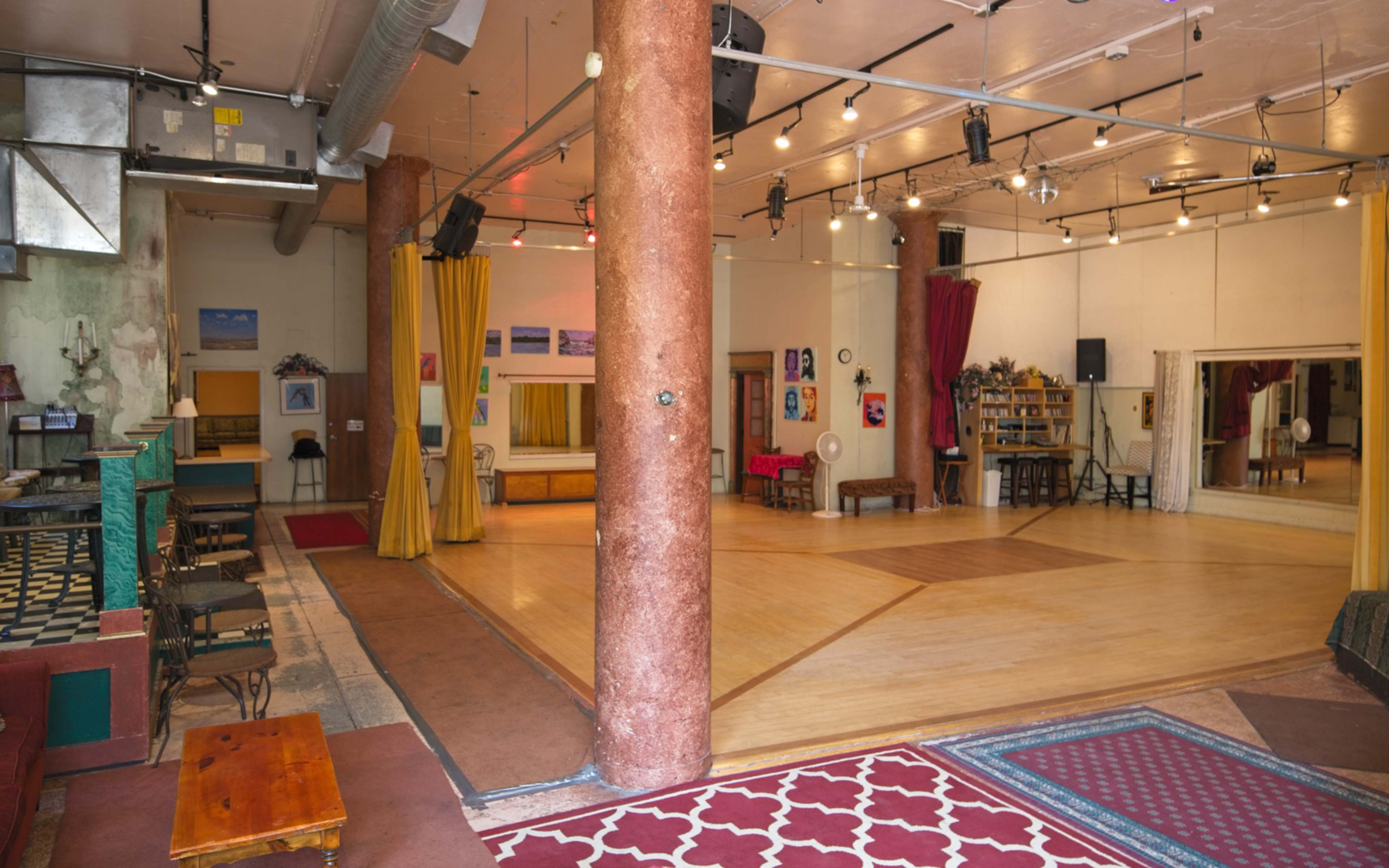 A spacious dance studio with wooden floors, large mirrors, and various seating areas, illuminated by overhead lights.