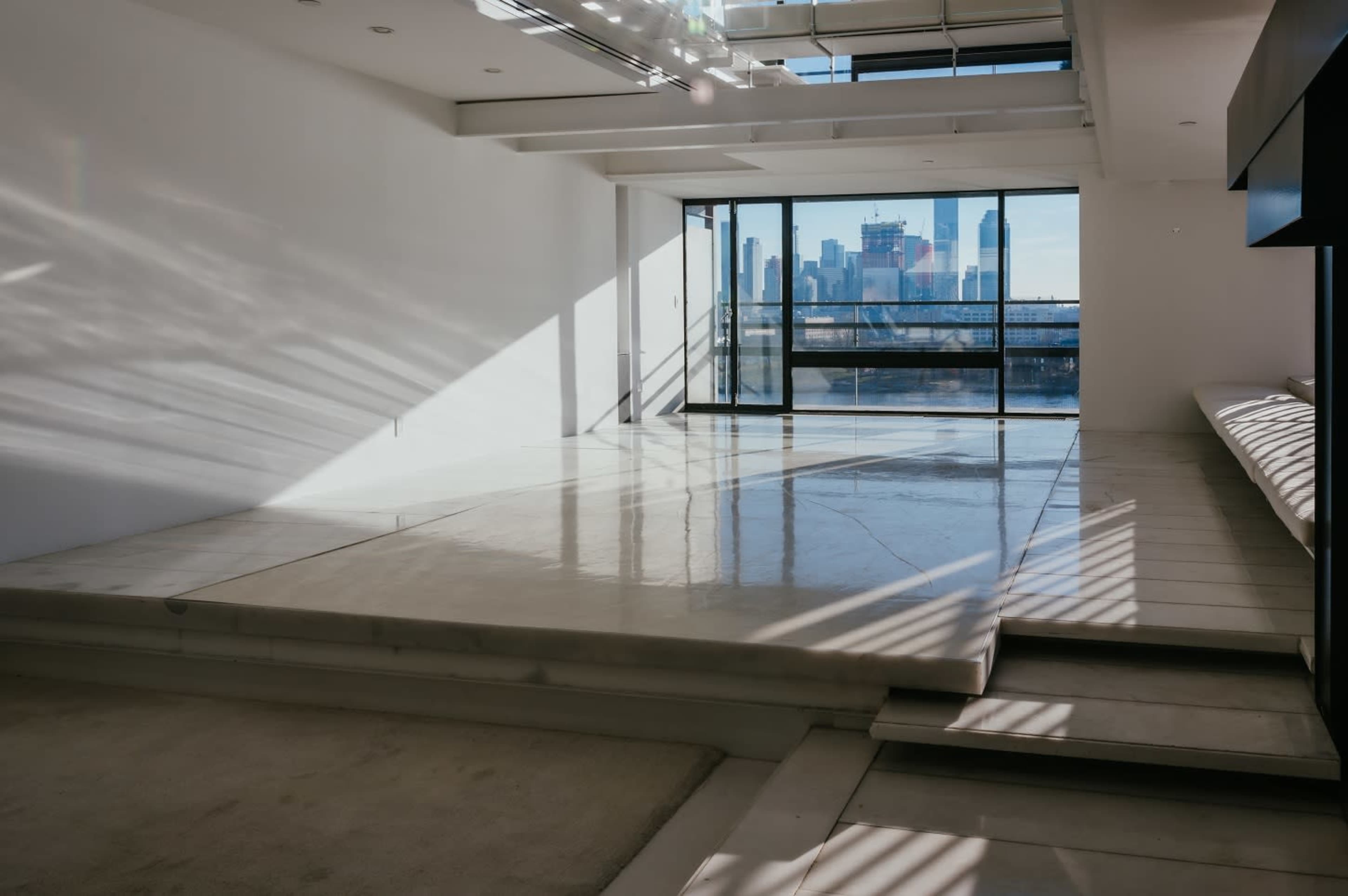 The image shows a spacious, modern room with a polished concrete floor and large windows overlooking a city skyline.