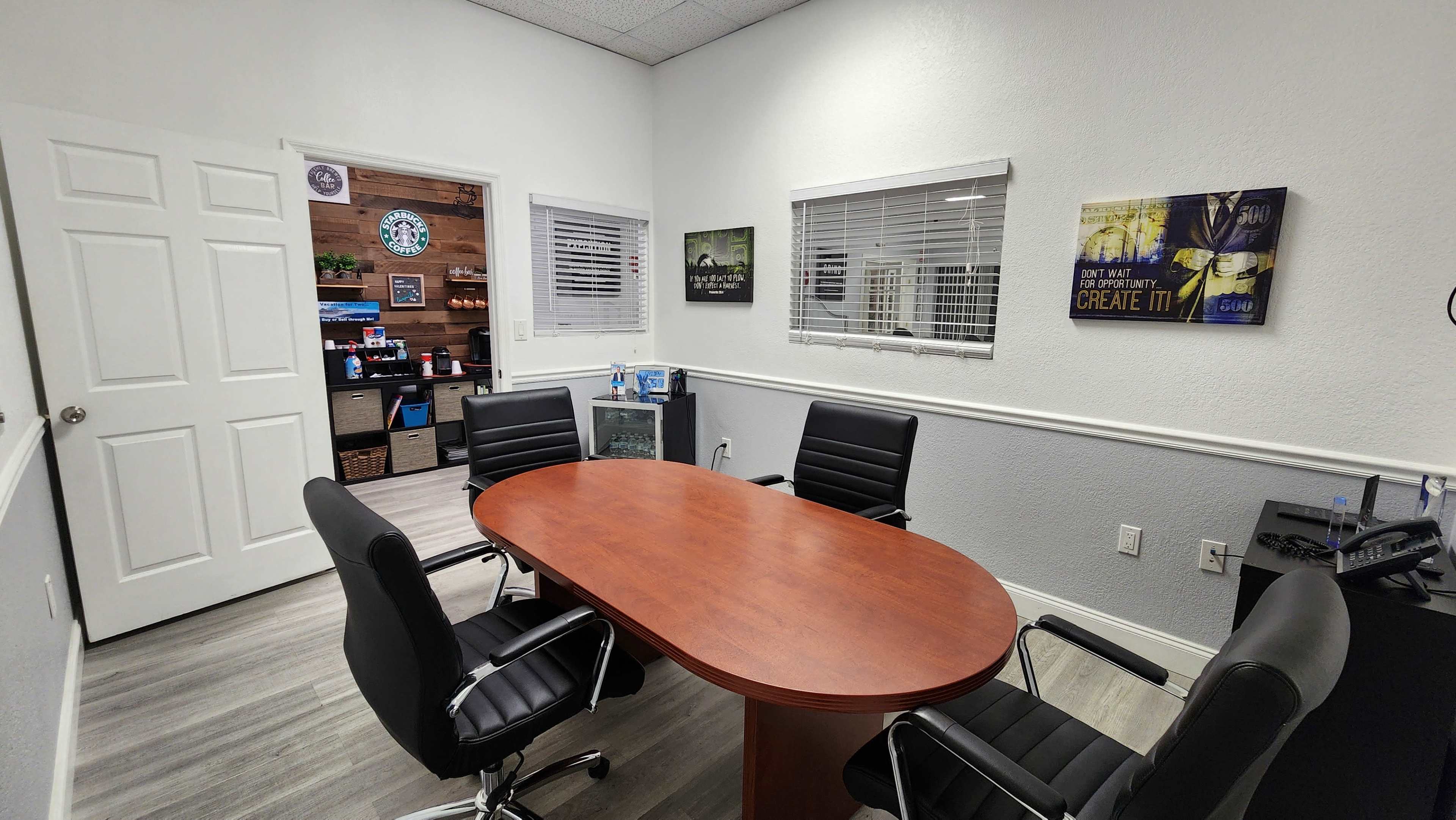 A conference room with a wooden oval table surrounded by four black chairs and a door leading to another room.
