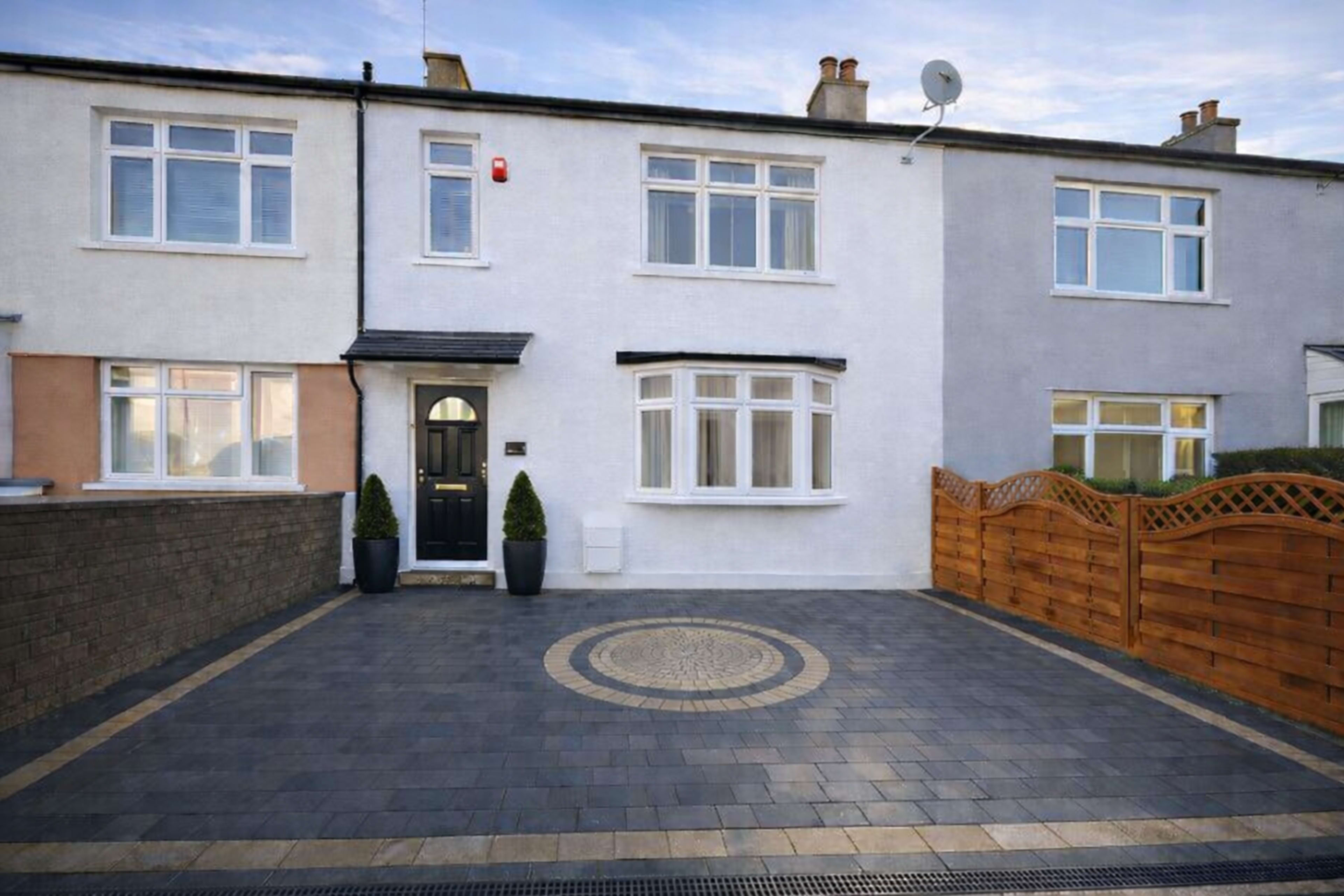 The image depicts a modern two-story house with a paved driveway and a wooden fence.