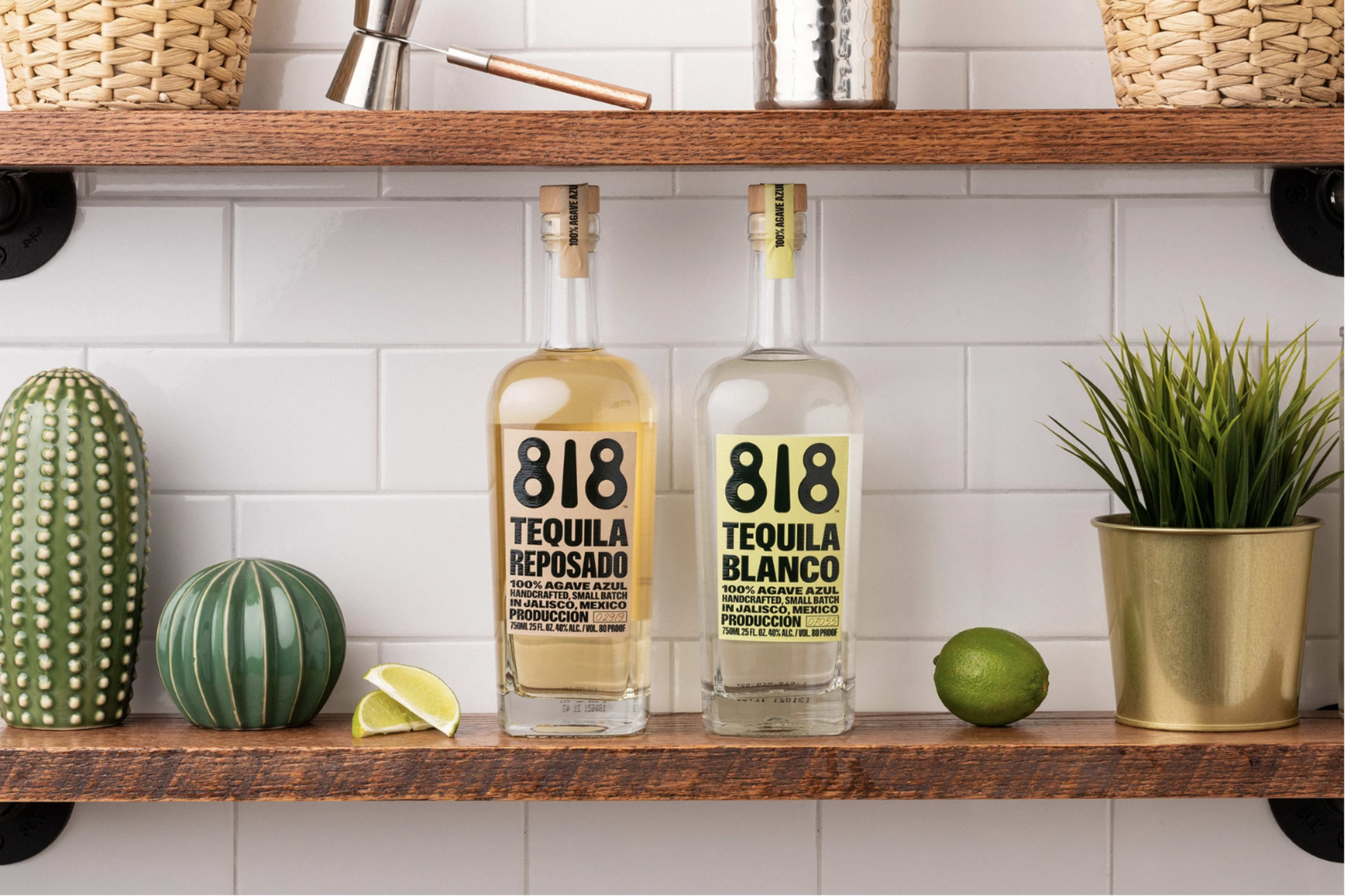 Two bottles of 818 tequila, one labeled "Reposado" and the other "Blanco," are displayed on wooden shelves alongside decorative items, including a green cactus and potted plants.
