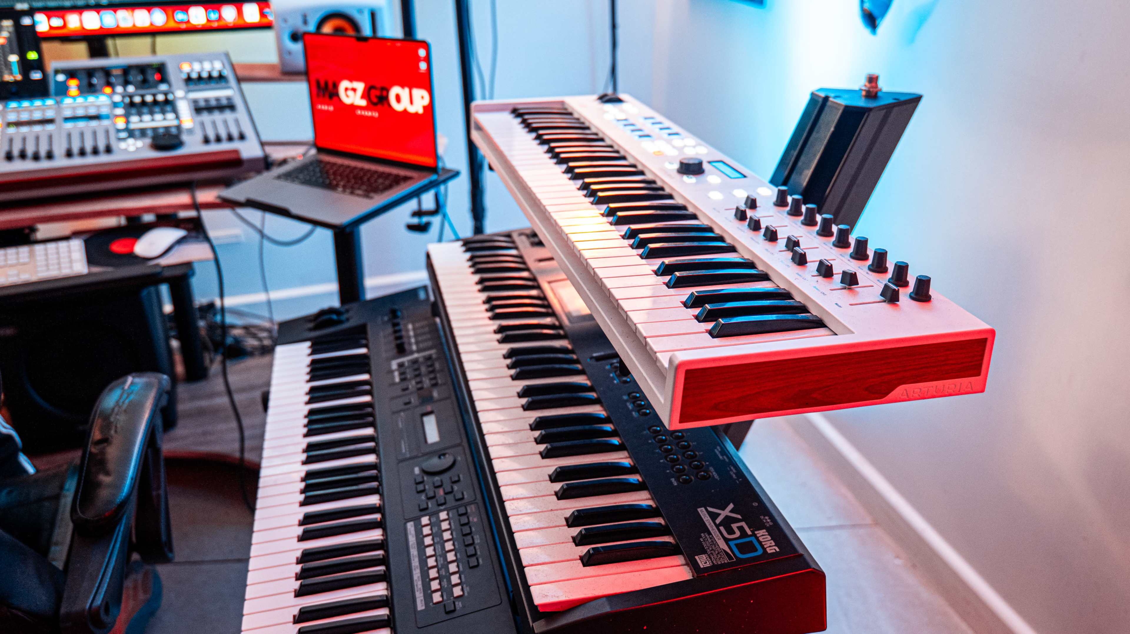 The image shows a modern music production setup featuring two keyboards stacked vertically, along with a laptop displaying software on a desk.