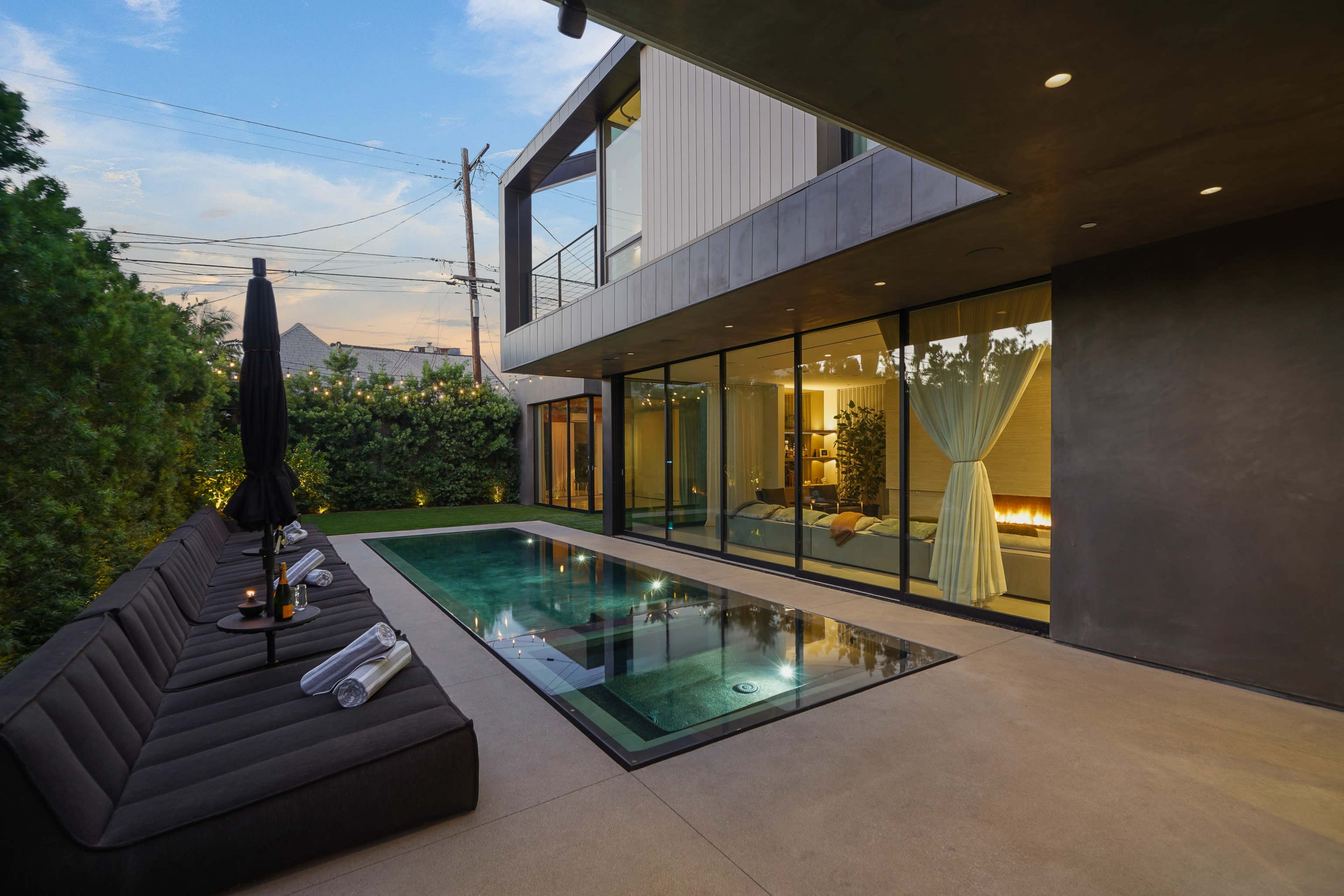 The image shows a modern outdoor area featuring a small pool, lounge seating, and large glass windows overlooking a contemporary interior space.