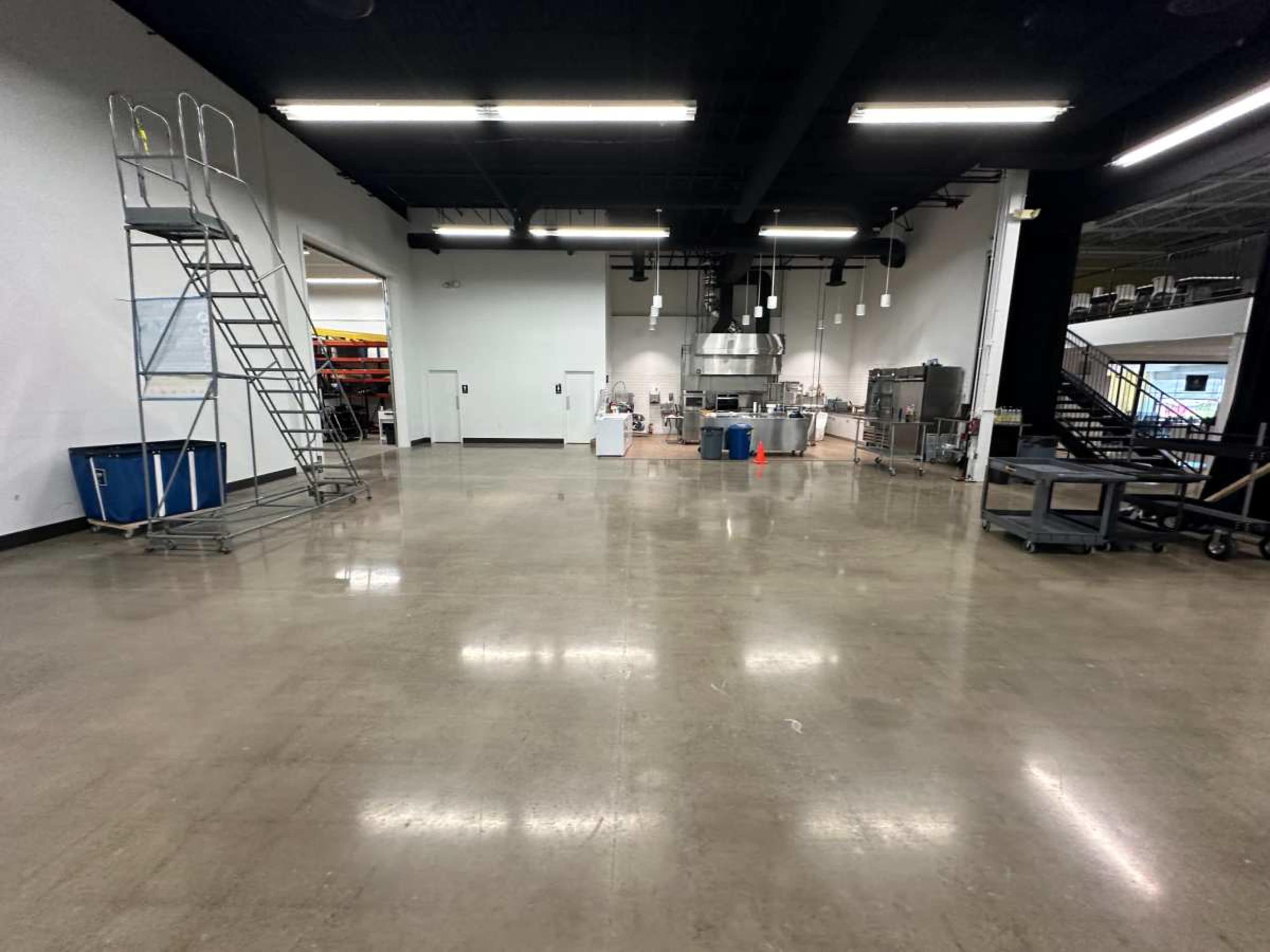 An empty commercial kitchen space with stainless steel appliances and a large ladder in the foreground.