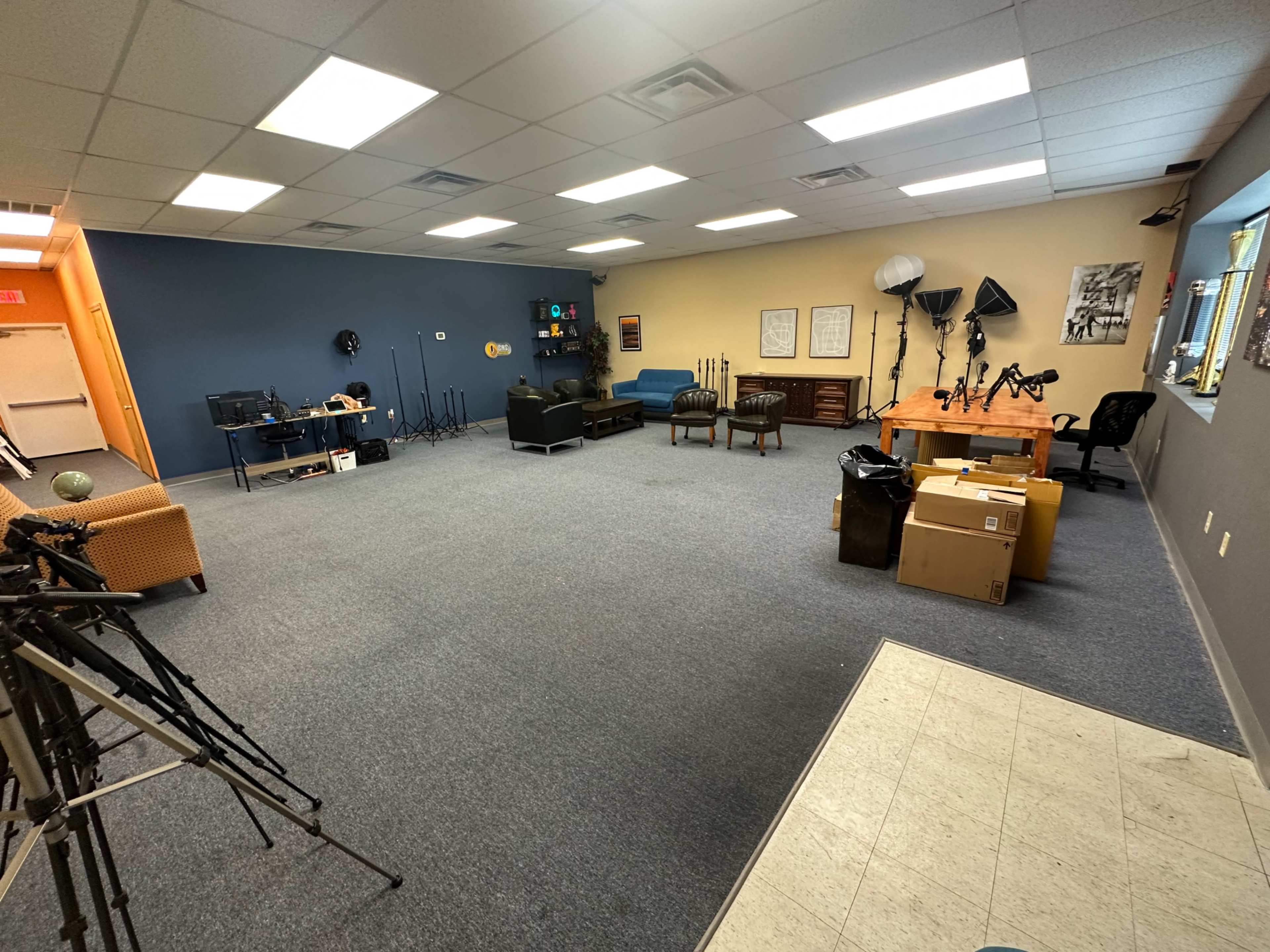 A spacious room with a blue and beige color scheme, containing seating areas, a desk, multiple tripods, and various equipment scattered around.