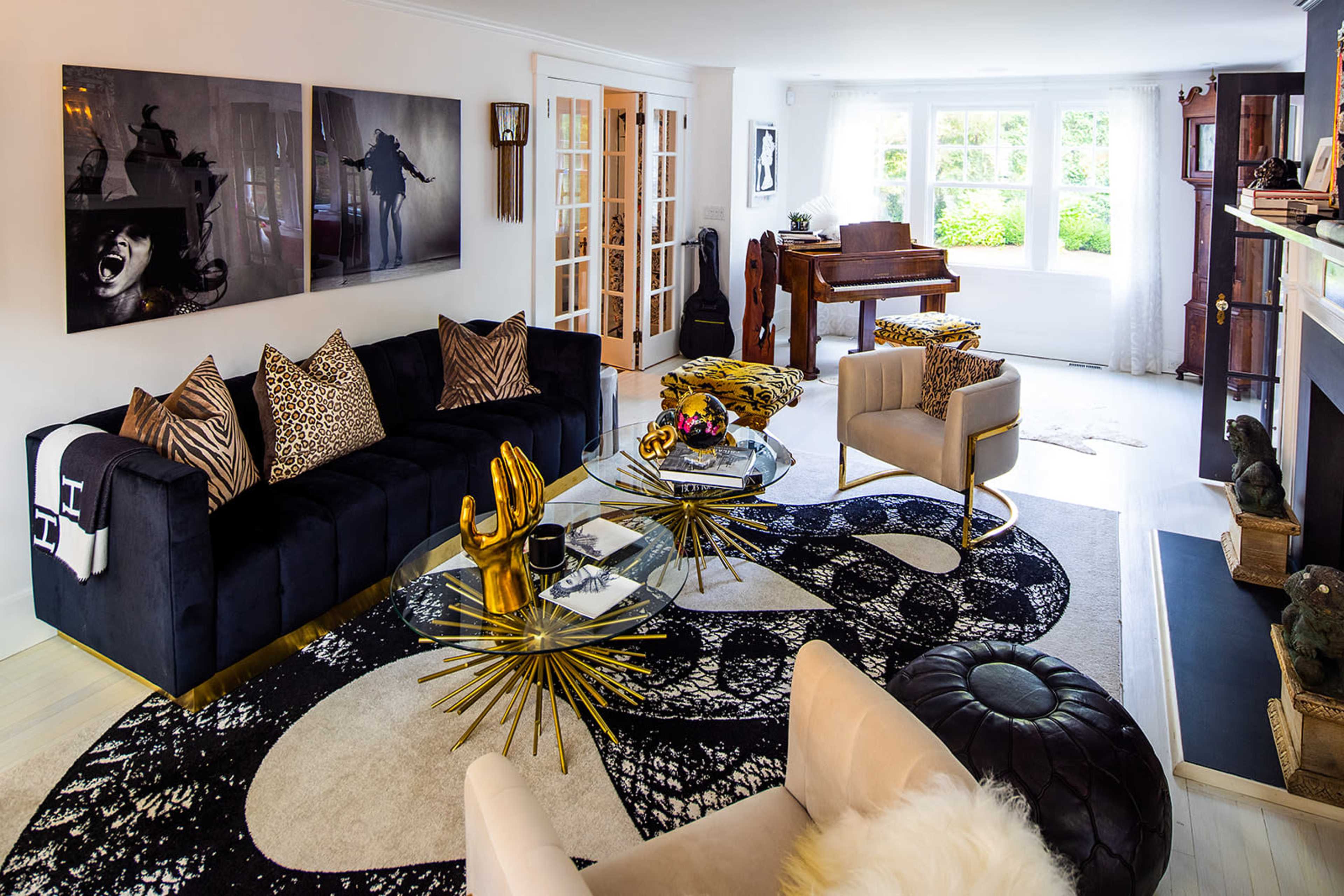 The image shows a modern living room with a black sofa, a round coffee table, and a grand piano, featuring large windows that let in natural light.