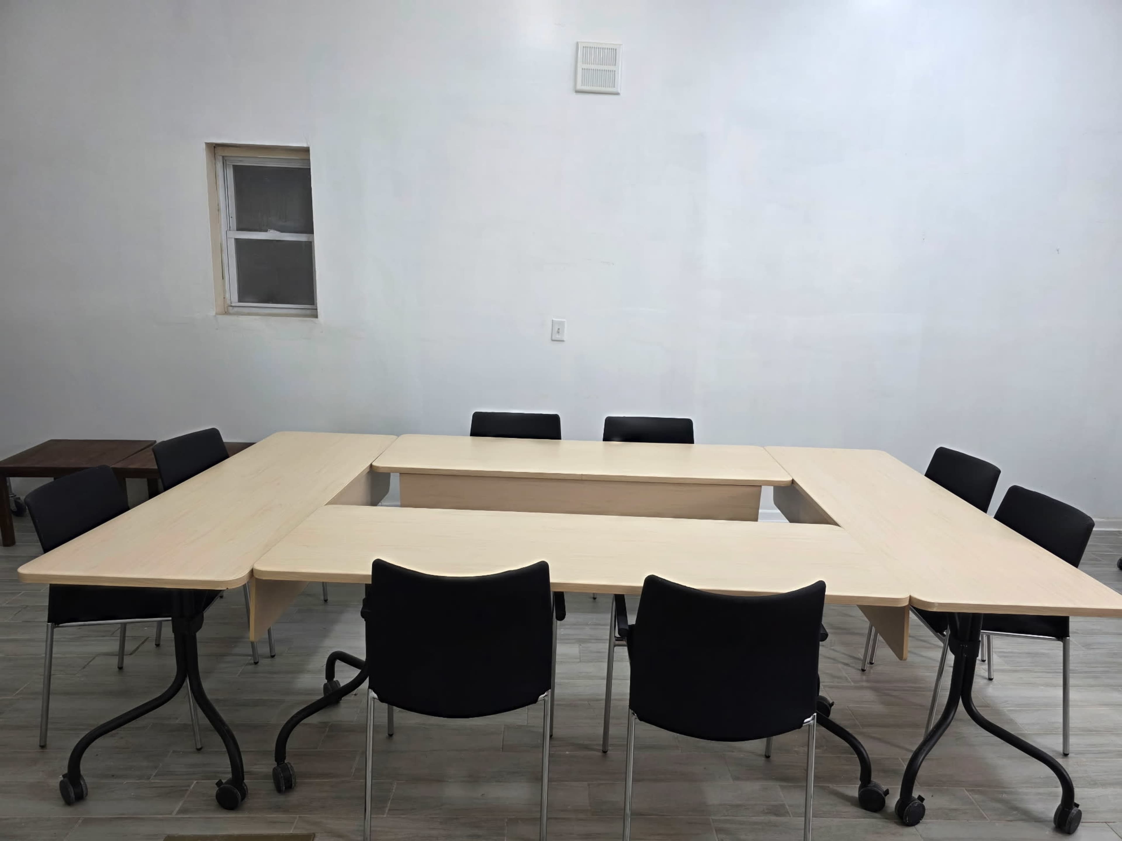 A rectangular meeting table is arranged in a U-shape with black chairs positioned around it in a sparsely furnished room.