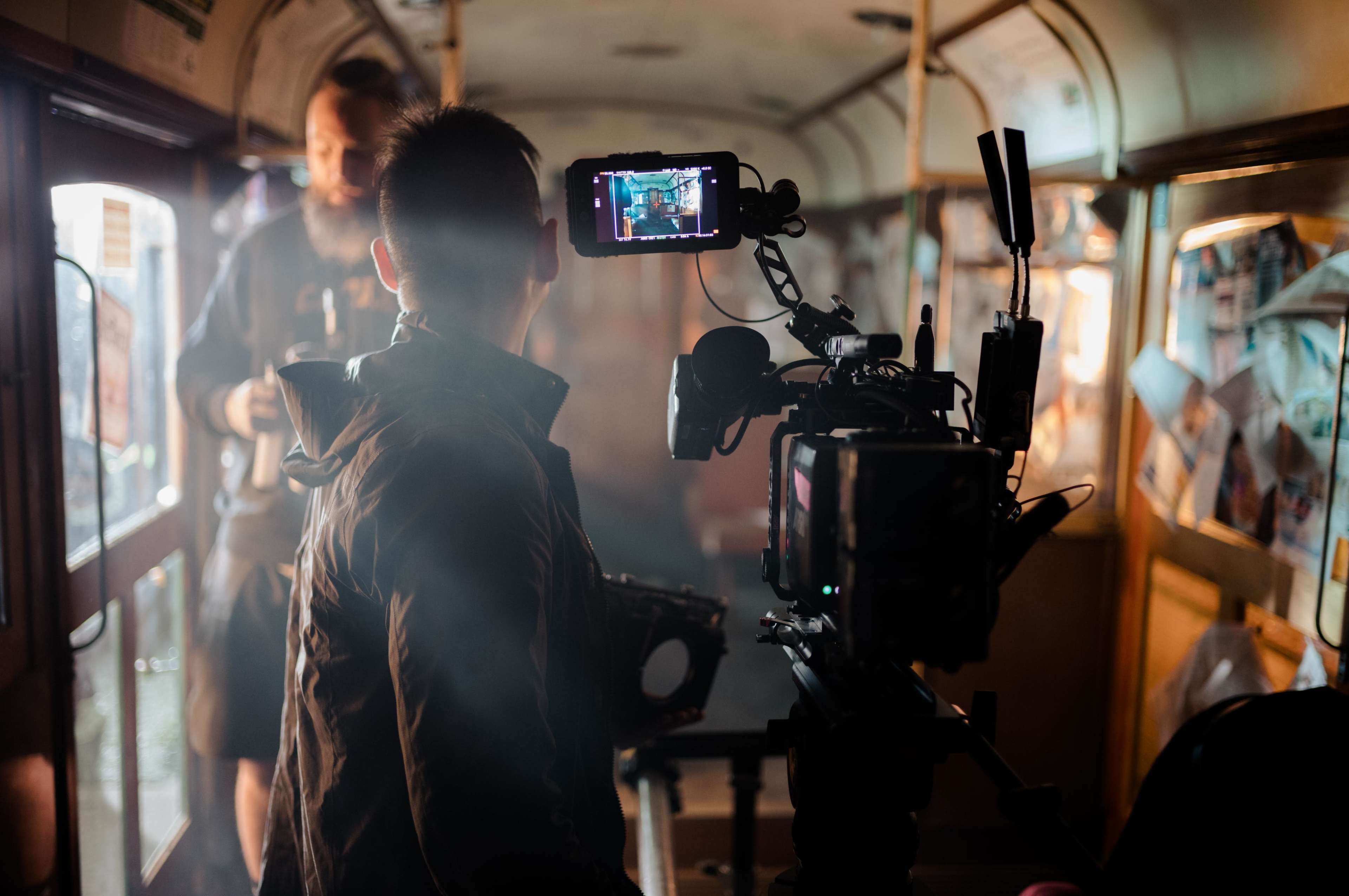 A camera operator records a scene inside an old train carriage, surrounded by smoke and crew members.