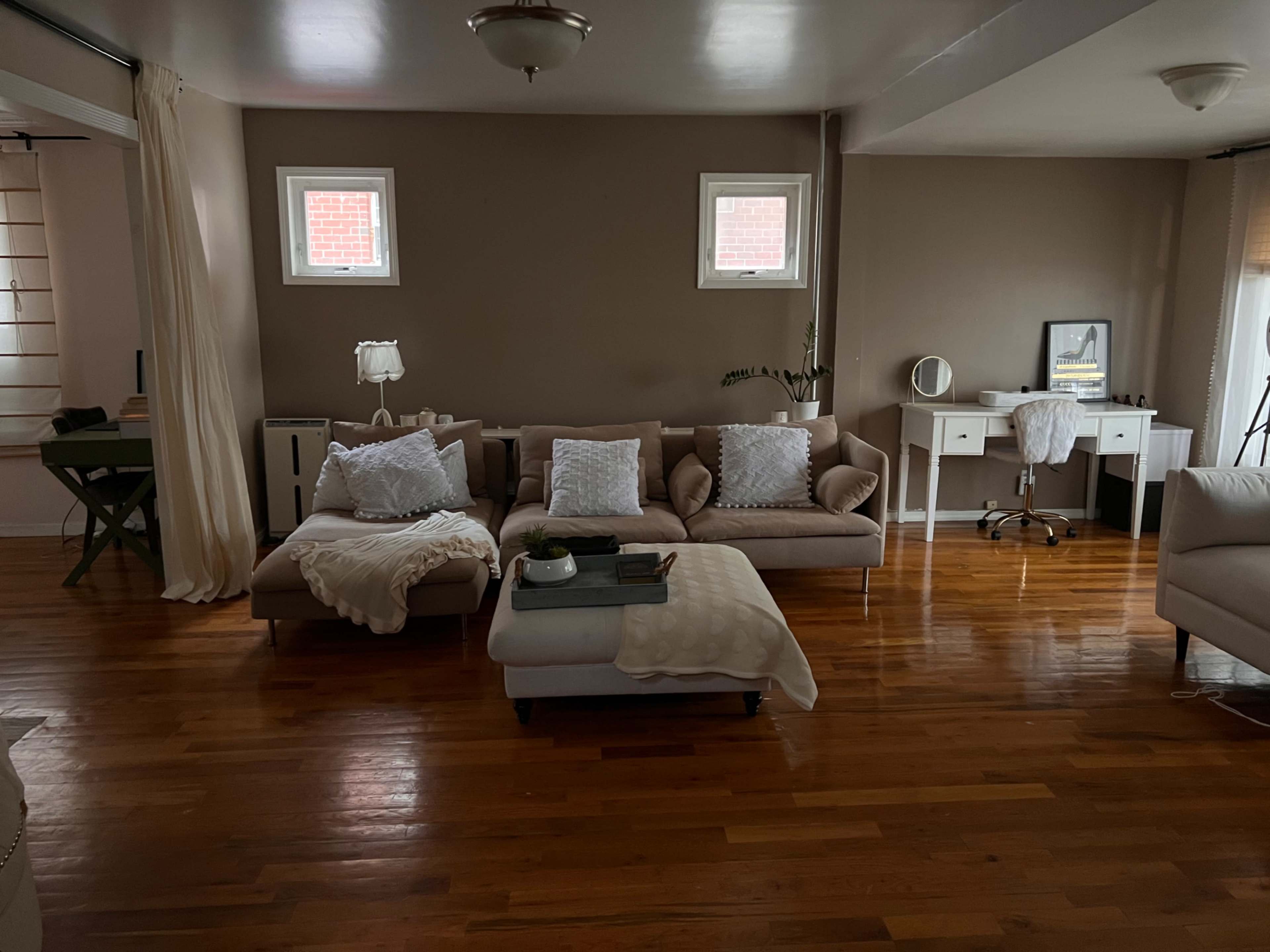 The living room features two sofas, a coffee table, and a desk, all set against a backdrop of hardwood floors and neutral-colored walls.