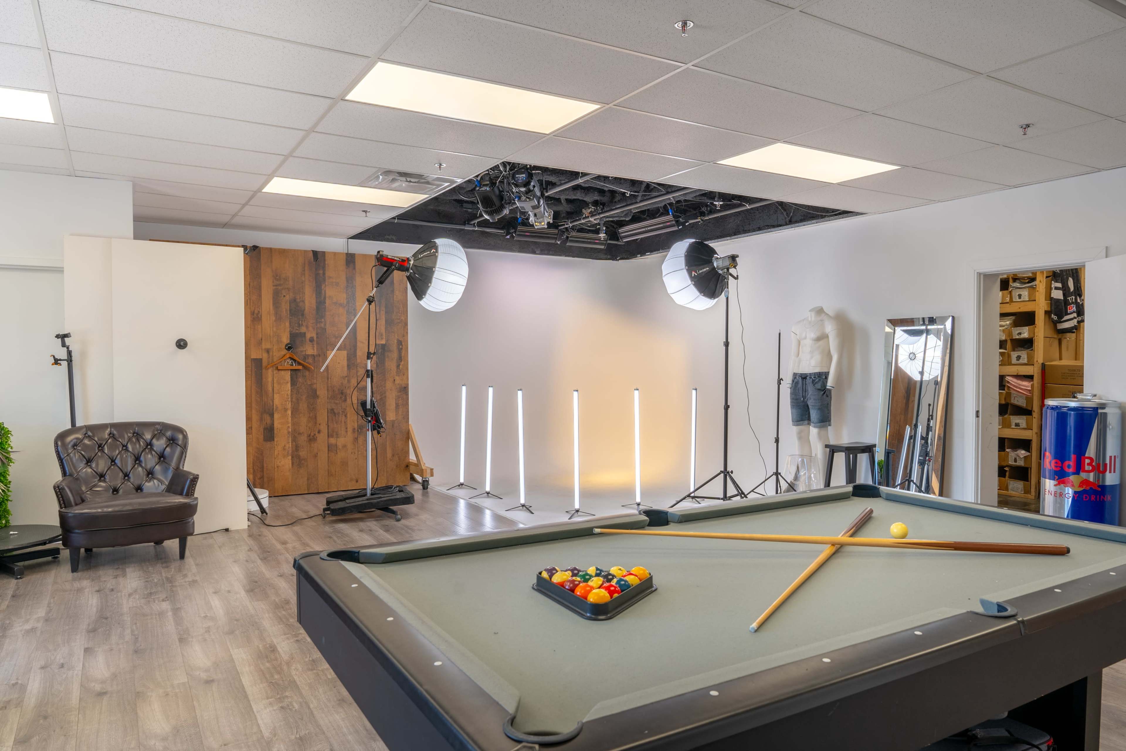 The image shows a billiards table with a set of colorful balls and cue sticks in a well-lit room featuring a backdrop setup and photography lighting equipment.