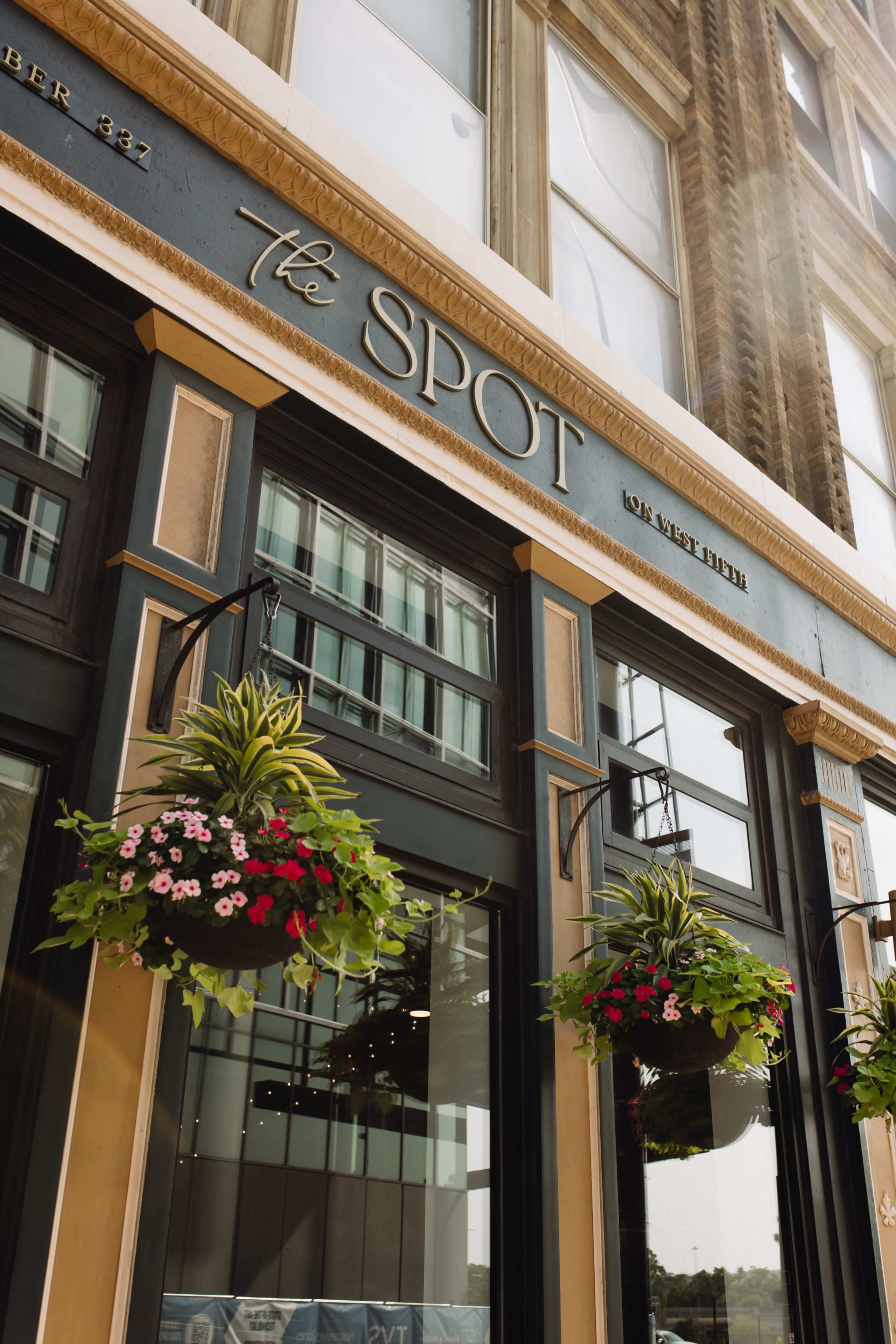 The image shows the entrance of a restaurant named "the SPOT" with hanging flower baskets and large windows.