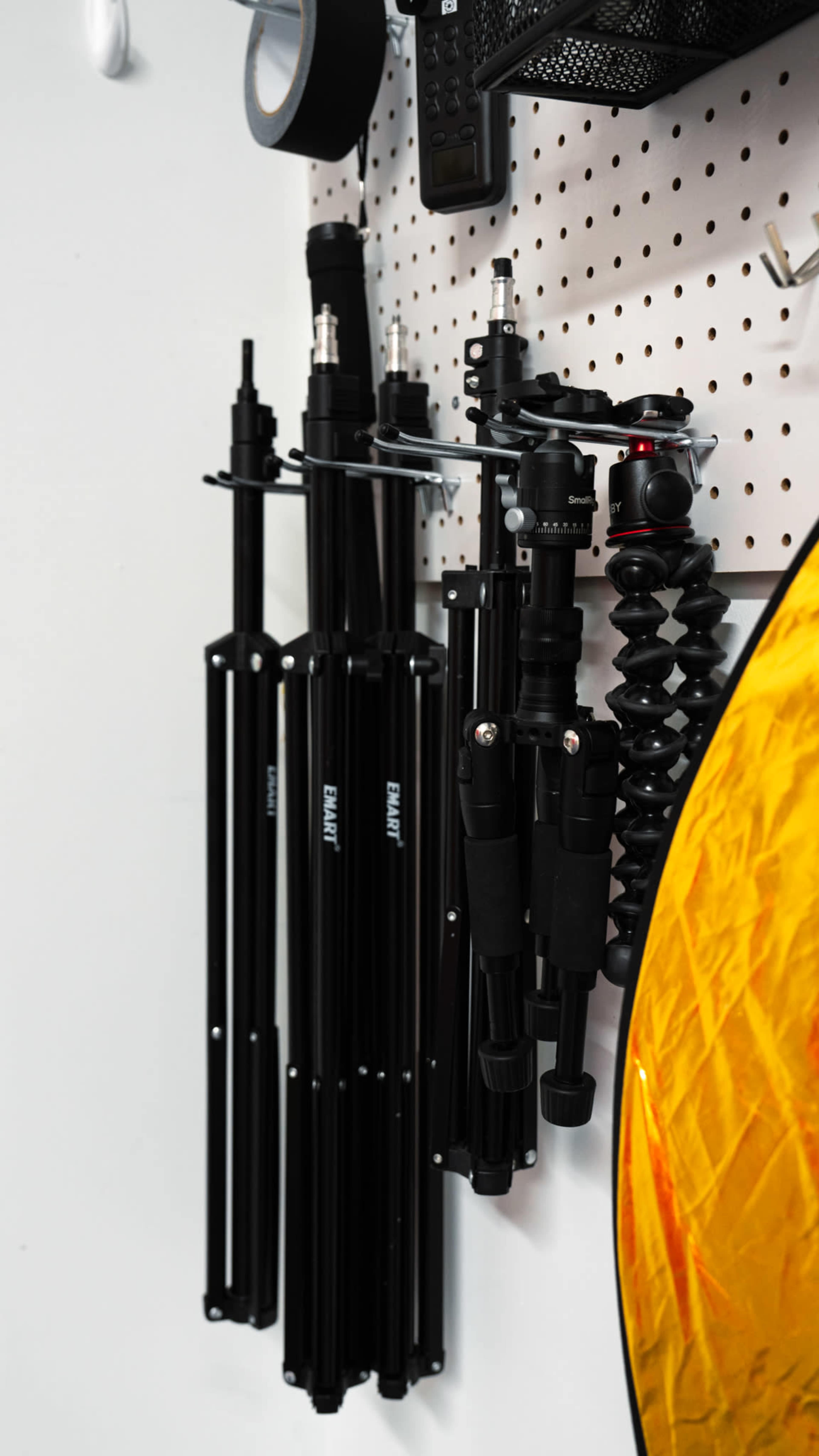 A collection of photography tripods and a reflector is neatly organized on a pegboard.
