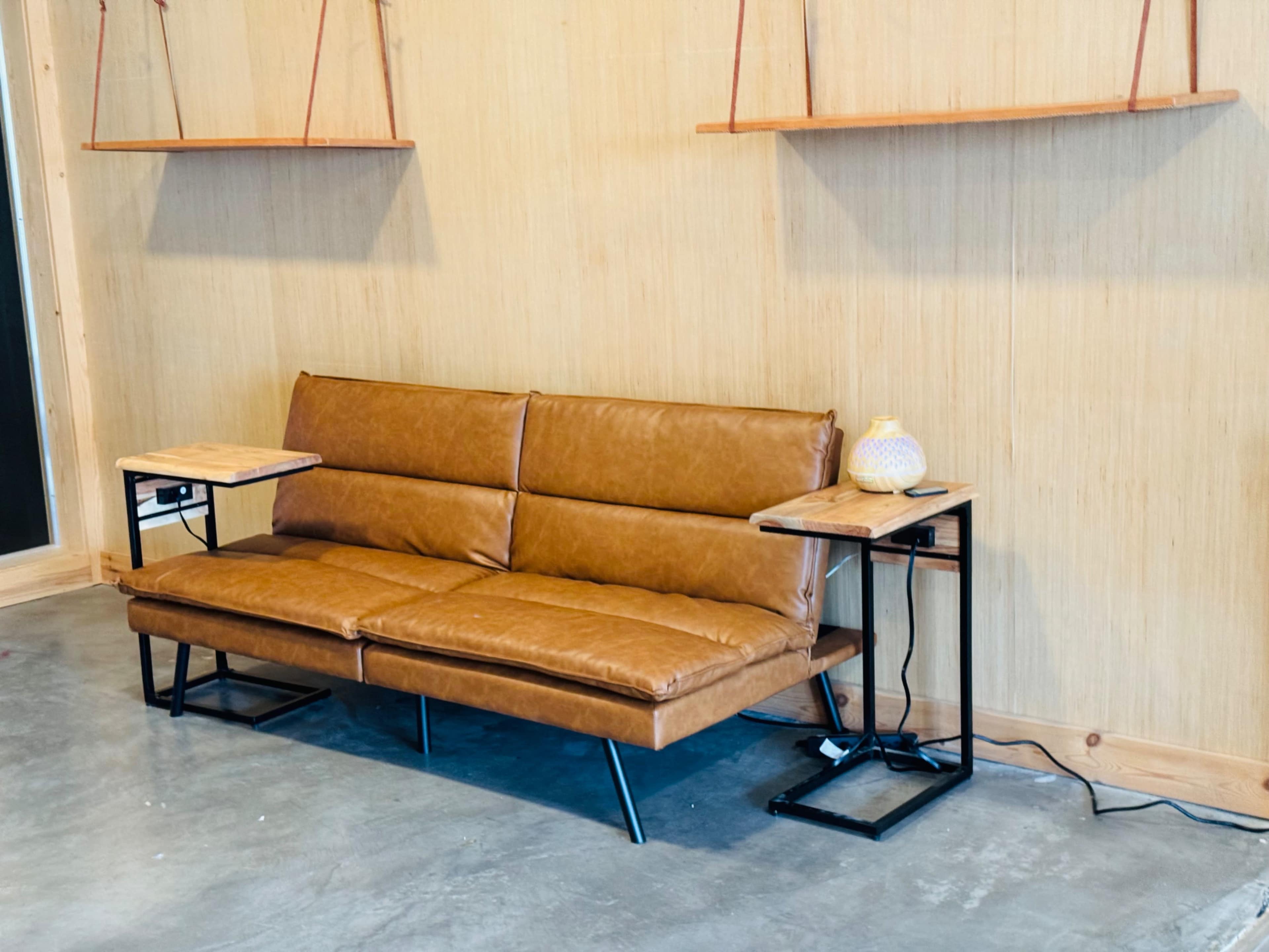 A brown leather sofa is positioned against a wooden wall, accompanied by two side tables with lamps on either side.