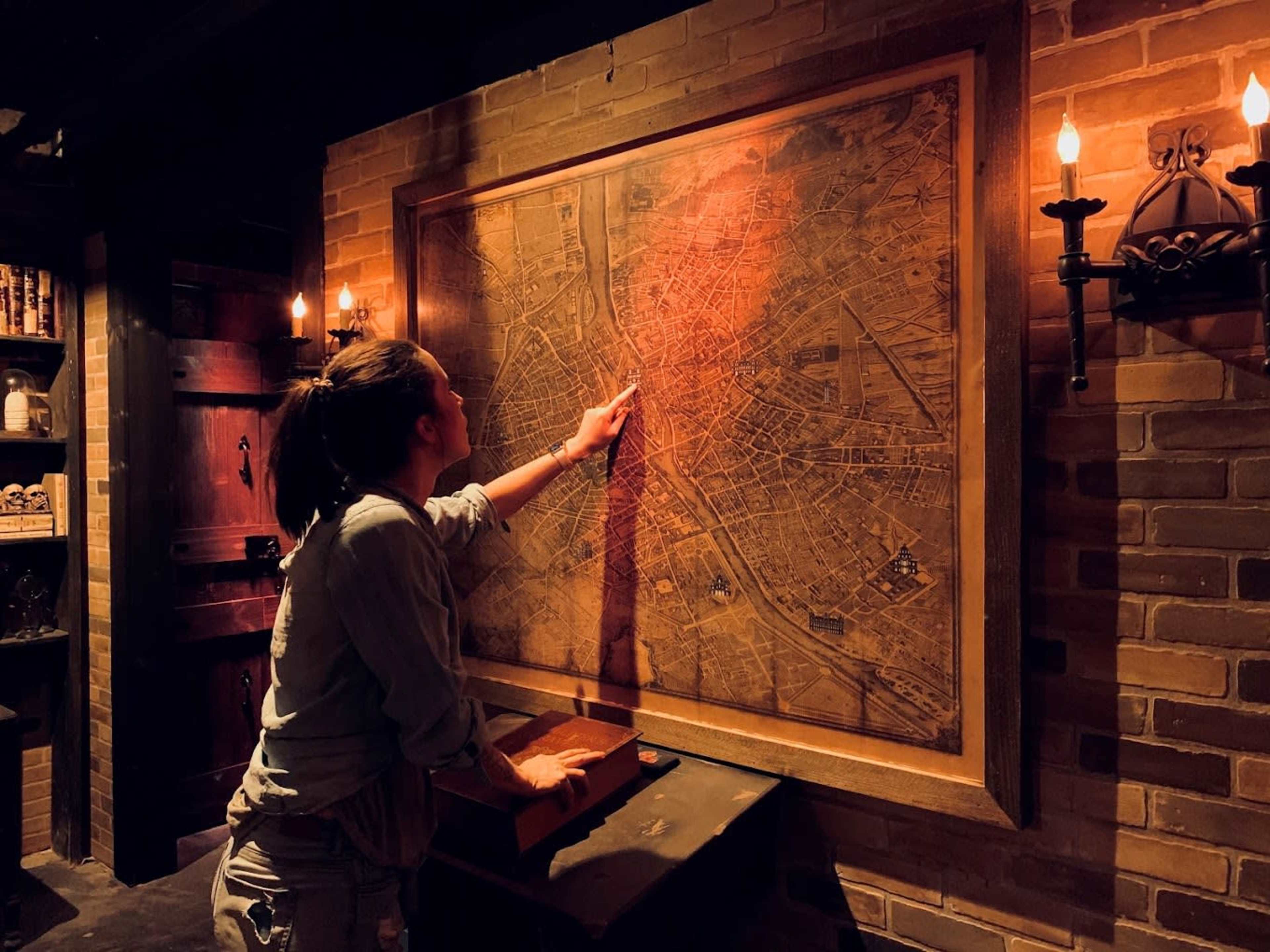 A person points at a vintage map mounted on a brick wall in a dimly lit room.