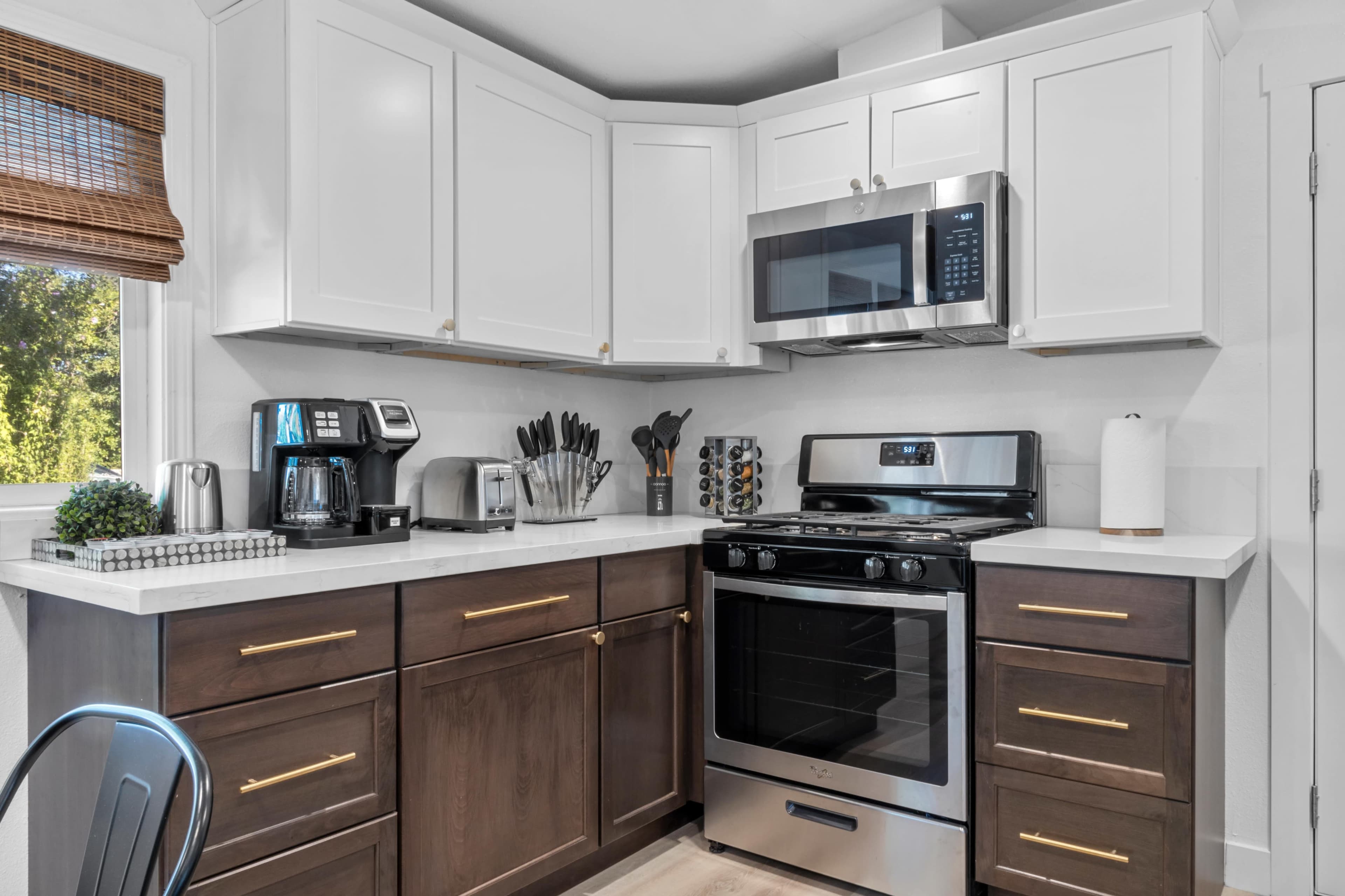 A modern kitchen with white upper cabinets, dark lower cabinets, a stainless steel stove, and a coffee maker on the countertop.