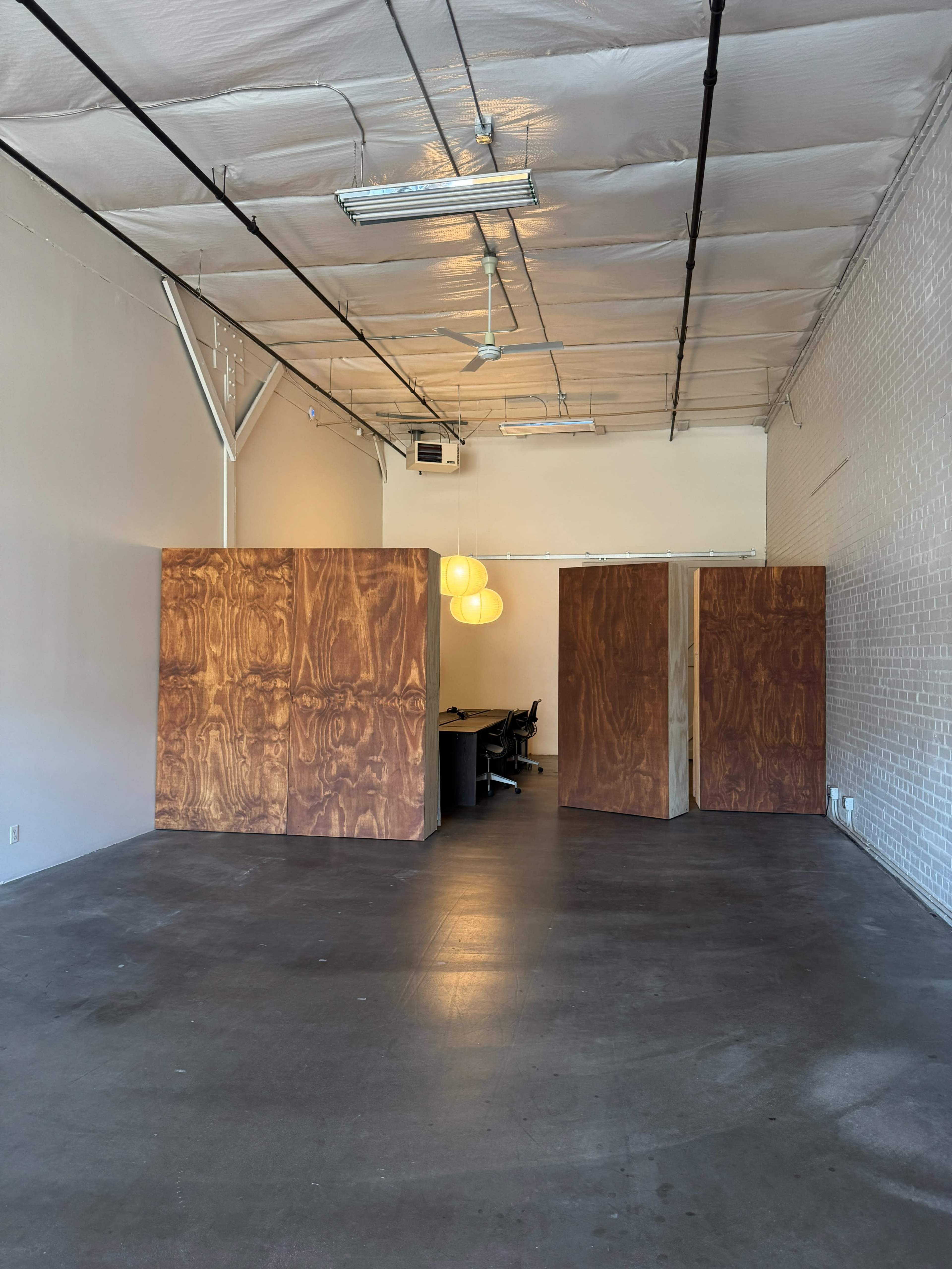 The image shows an empty office space with two wooden partitions, a conference table in the background, and three hanging light fixtures above.