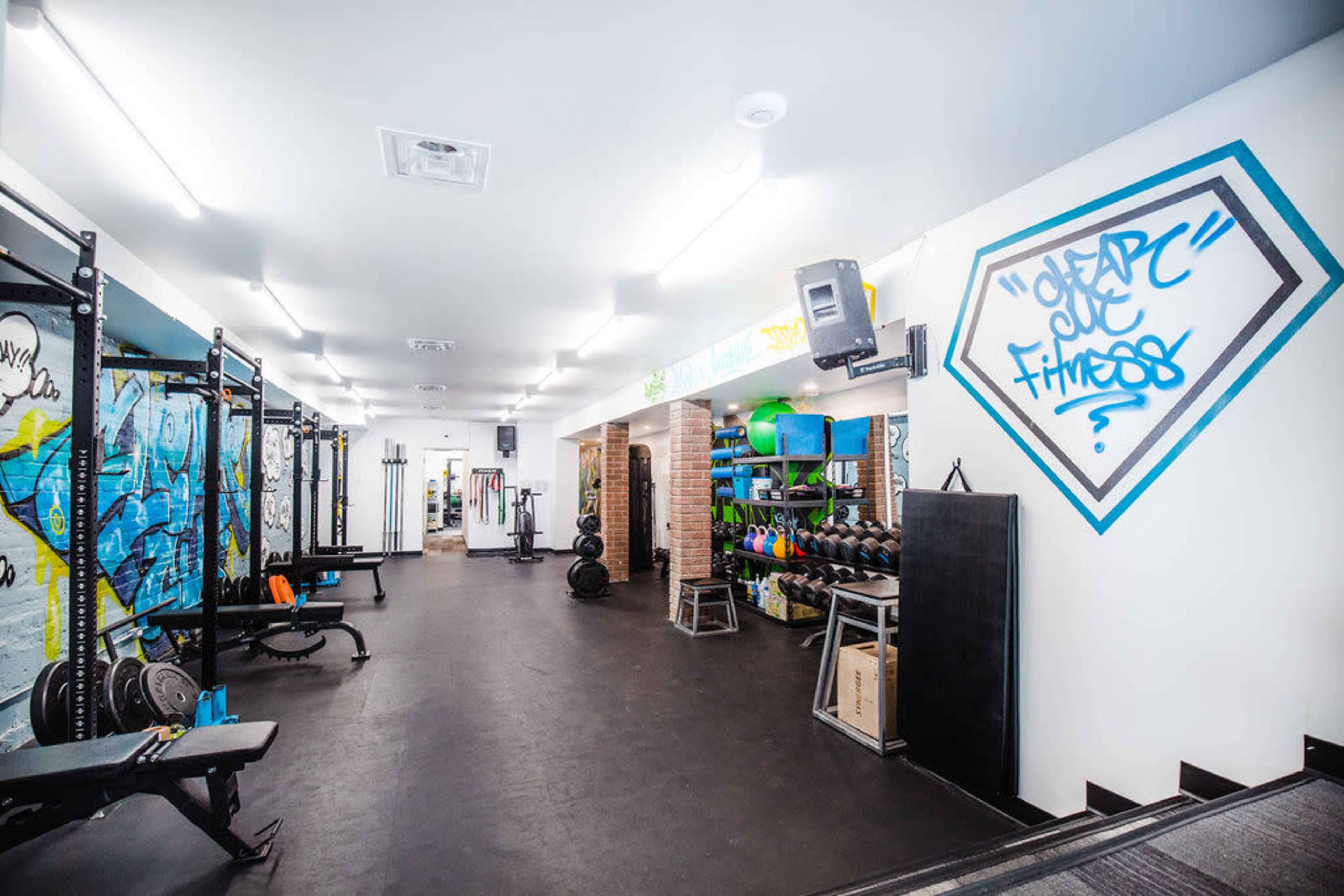 A gym interior featuring weightlifting equipment, a wall adorned with graffiti, and neatly organized fitness gear on shelves.