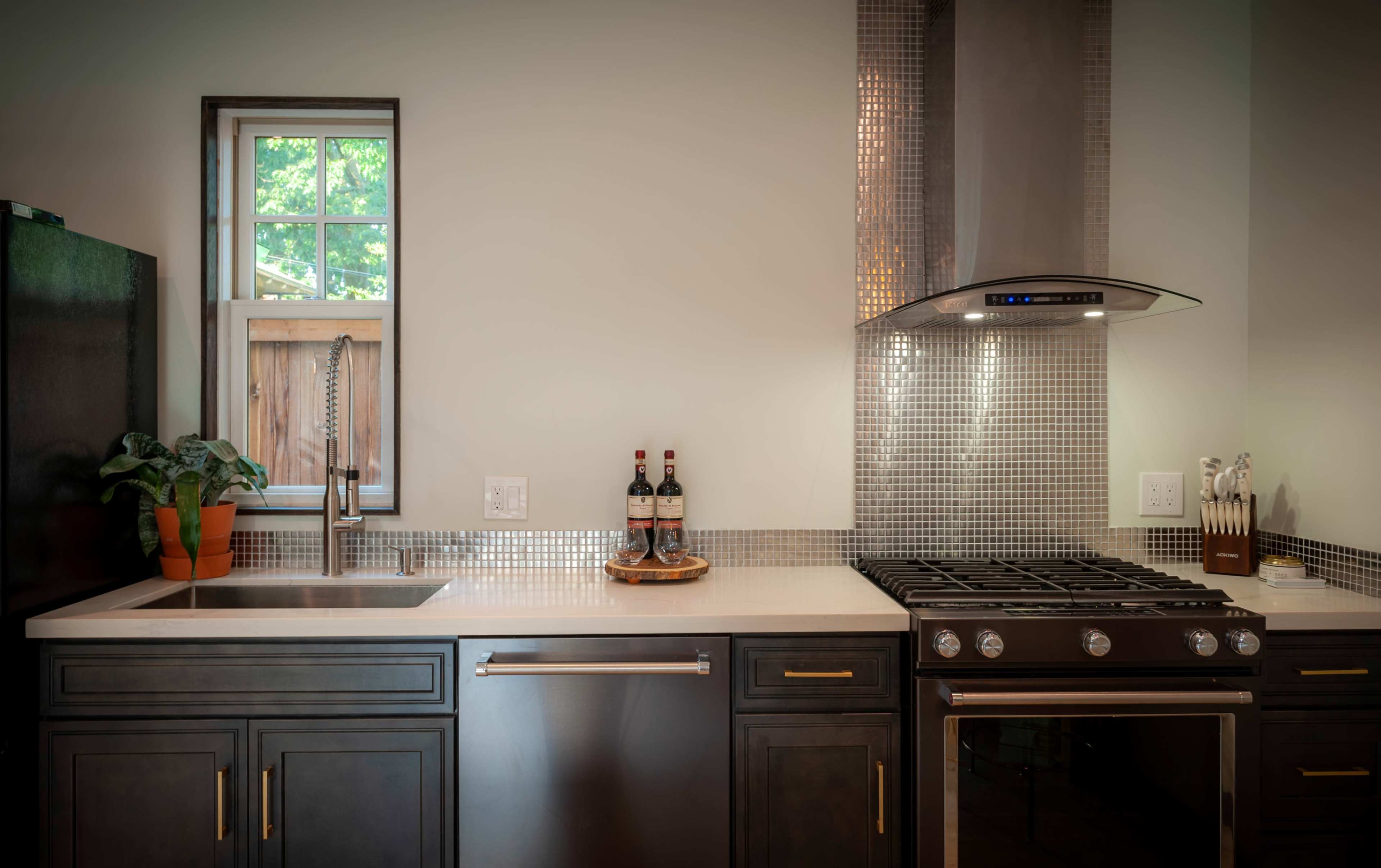 A modern kitchen features a stainless steel sink, a gas stove, and a mosaic tile backsplash with a window above the sink.